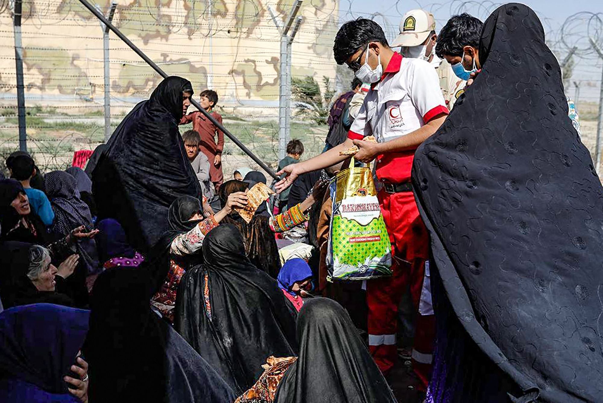 A member of the Iranian Red Crescent distributing food to Afghan refugees gathered at the Iran-Afghanistan border