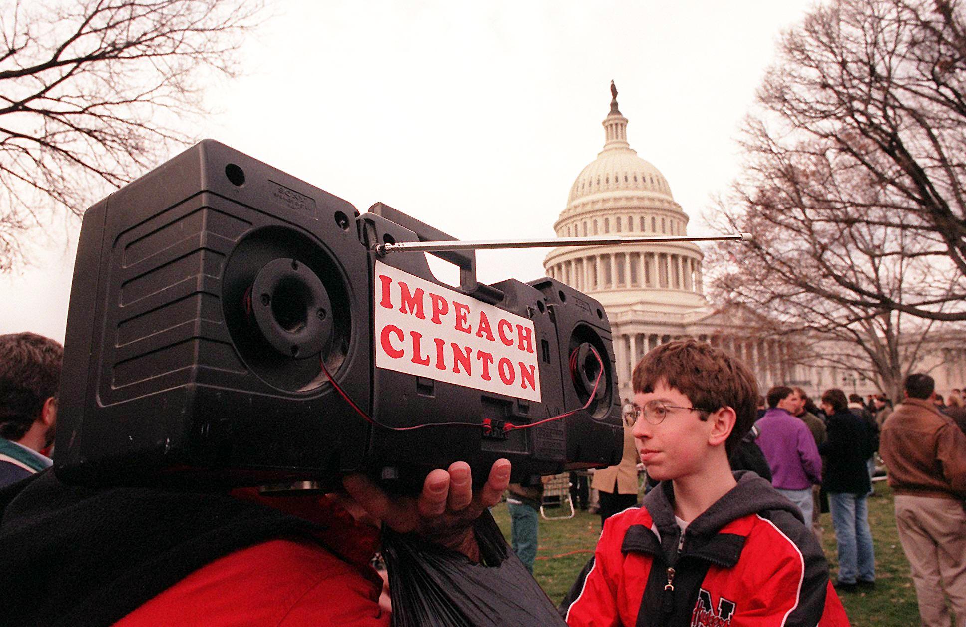 A man shoulders a portable radio with the words ‘Impeach Clinton’ pasted on its side as the US House of Representatives votes on the articles of impeachment against US president Bill Clinton on 19 December 1998 at the Capitol