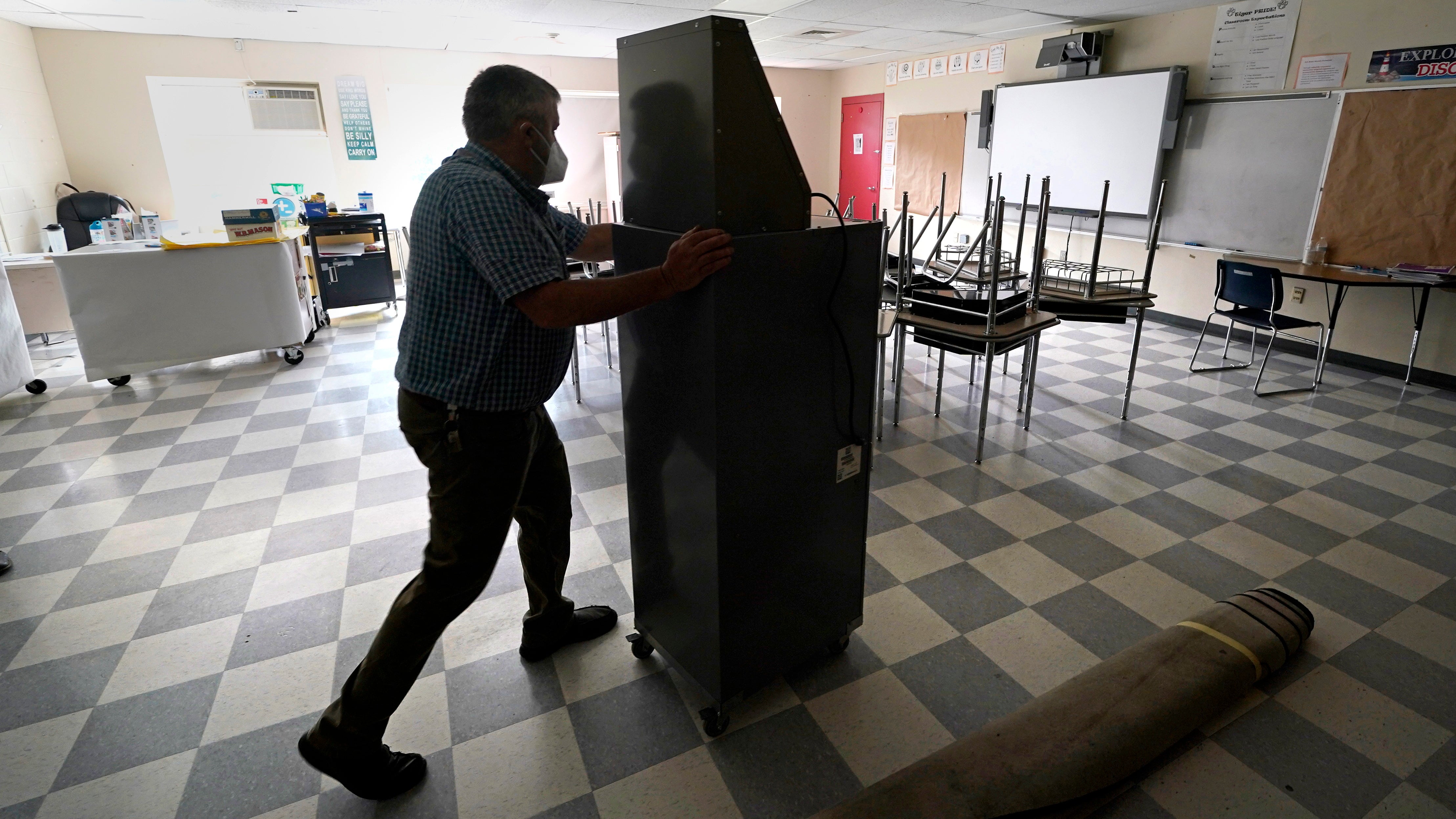 A man wheels a recently purchased air scrubber through a classroom in advance of the school year at a Massachusetts school.