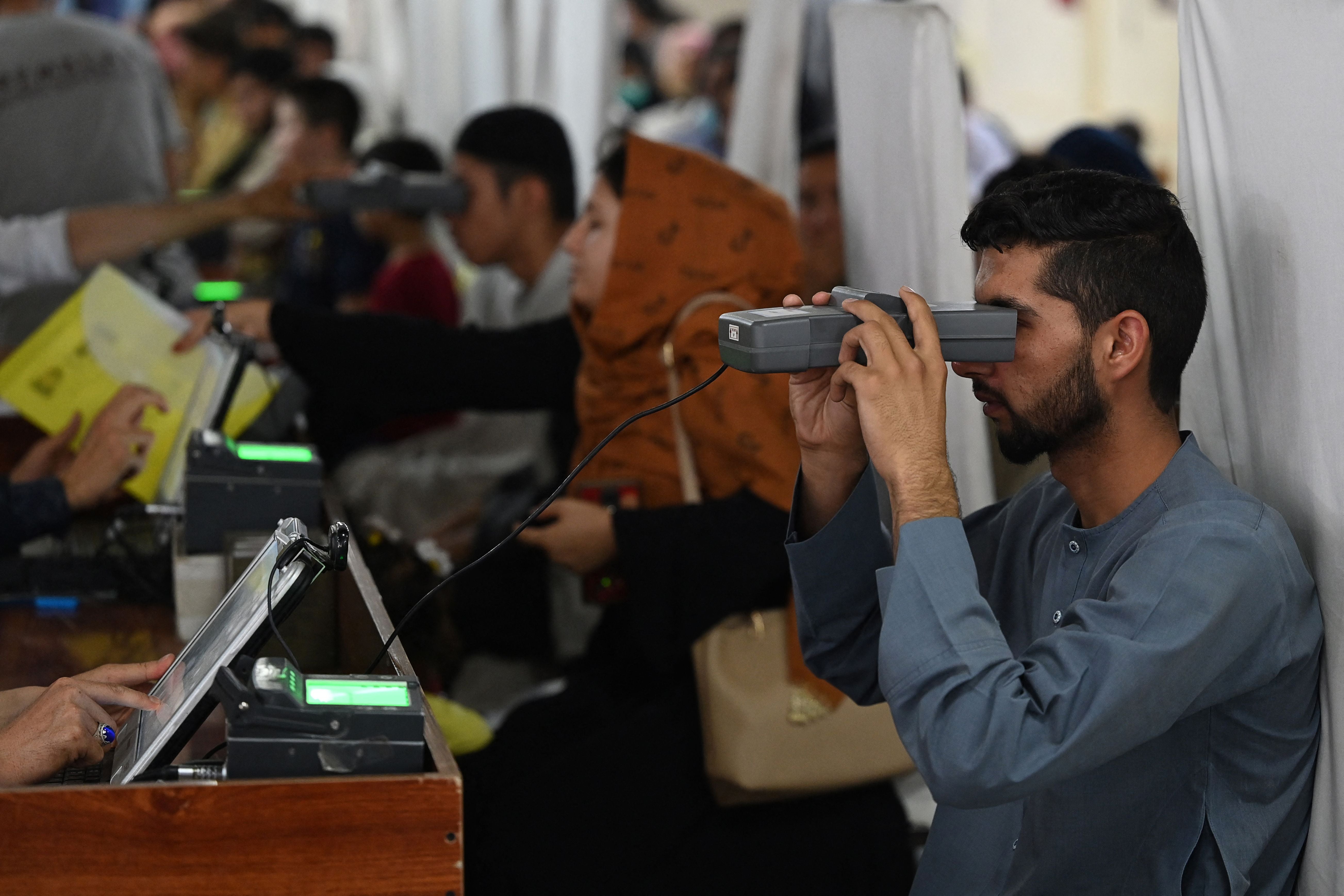 File: A man looks through an optical biometric reader to submit his passport application at an office in Kabul on 25 July 2021