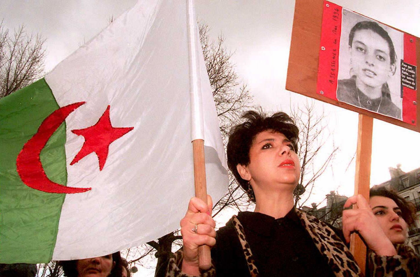 A woman in Paris carries an Algerian flag and the portrait of a victim of violence