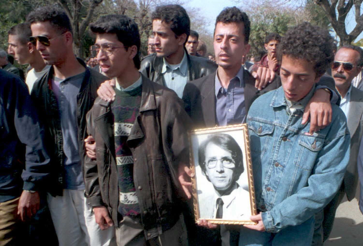 The three sons of Mohammed Abderrahamni, the assassinated editor-in-chief of the Algerian government daily El Moudjahid, carry a portrait of their father during his funeral