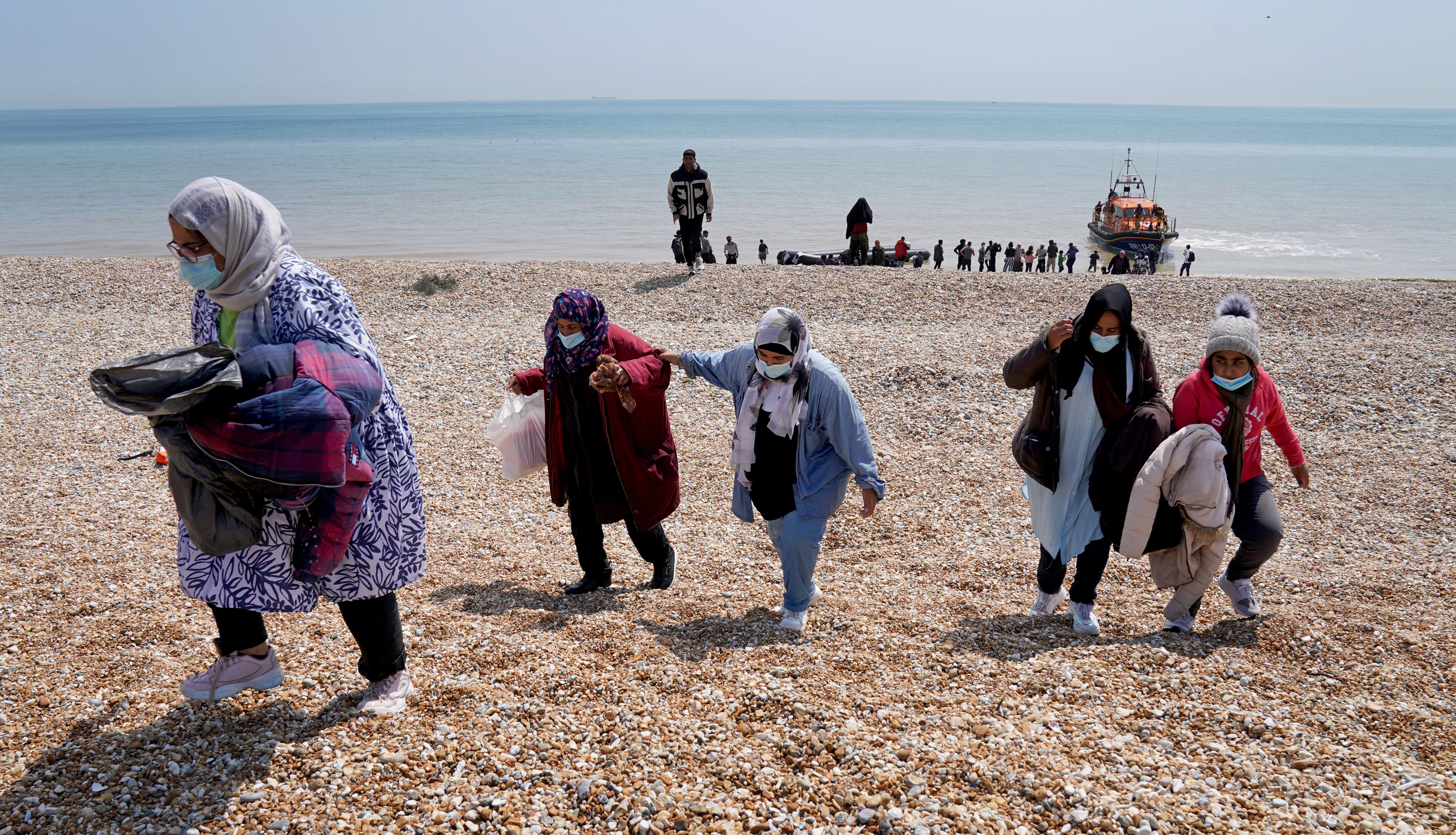 Migrants make their way up the beach after arriving on a small boat at Dungeness, in Kent, in July