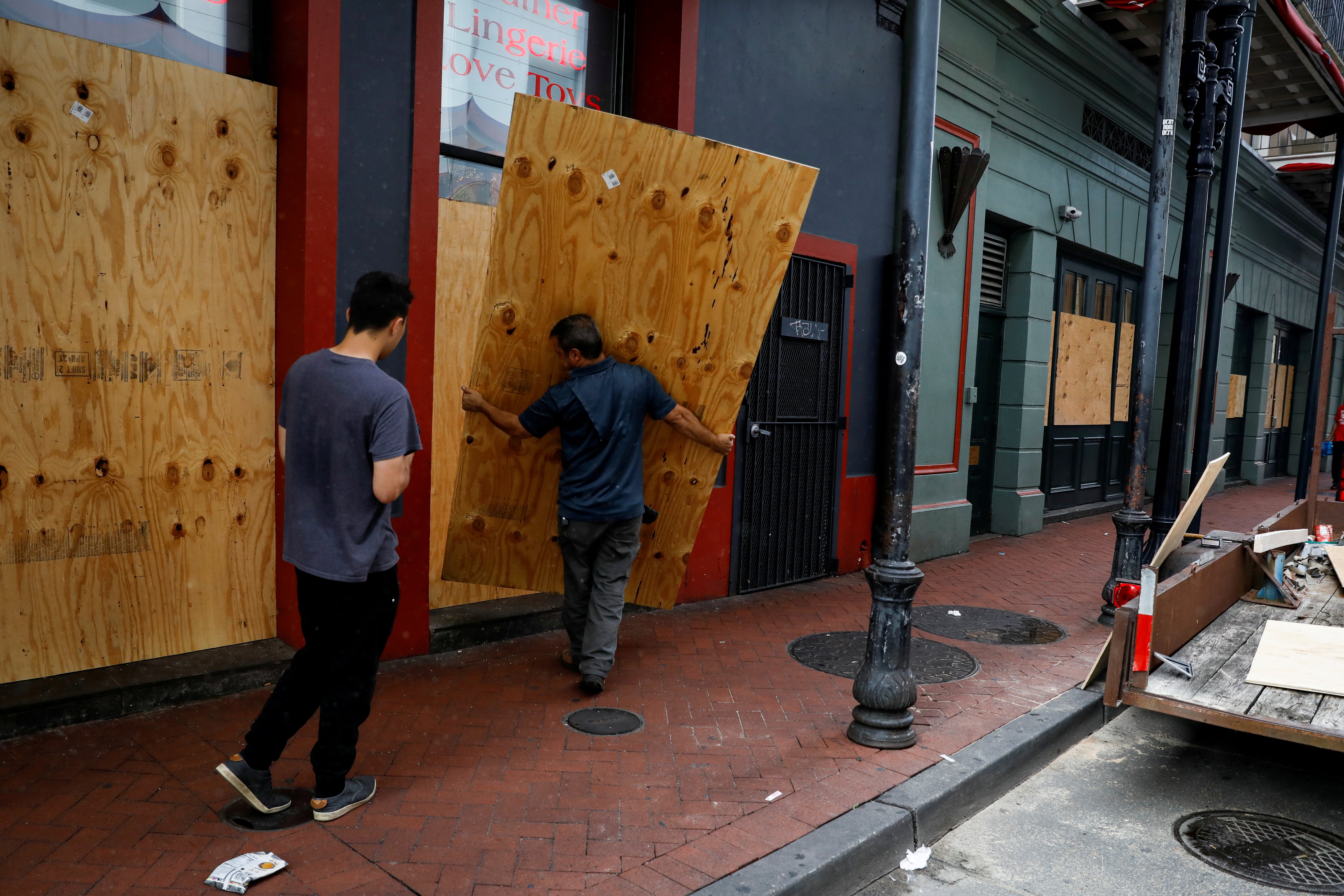 Men place plywood in front of a store in preparation for Hurricane Ida, in New Orleans