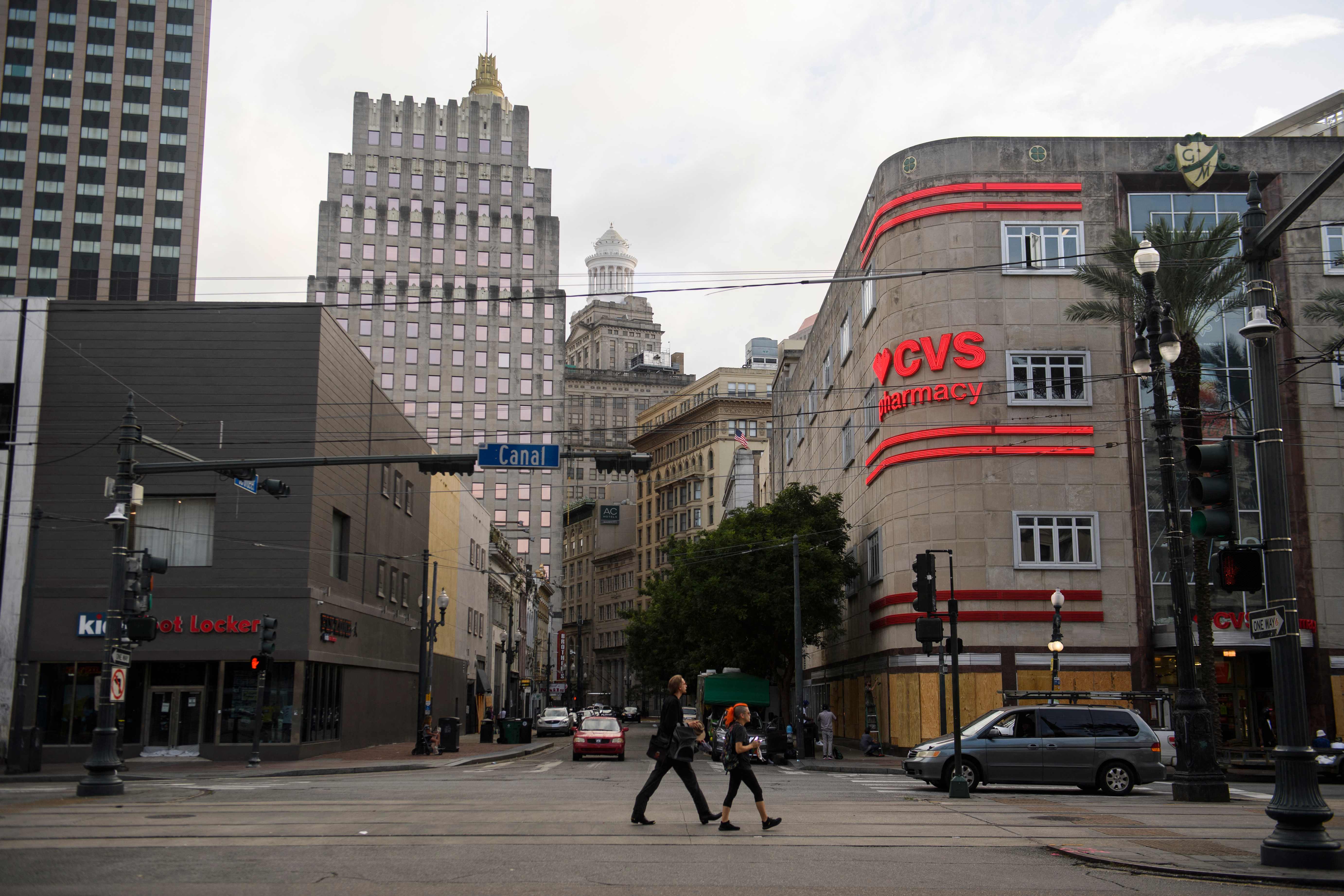 People walk down Canal Street past a boarded up CVS Pharmacy in New Orleans