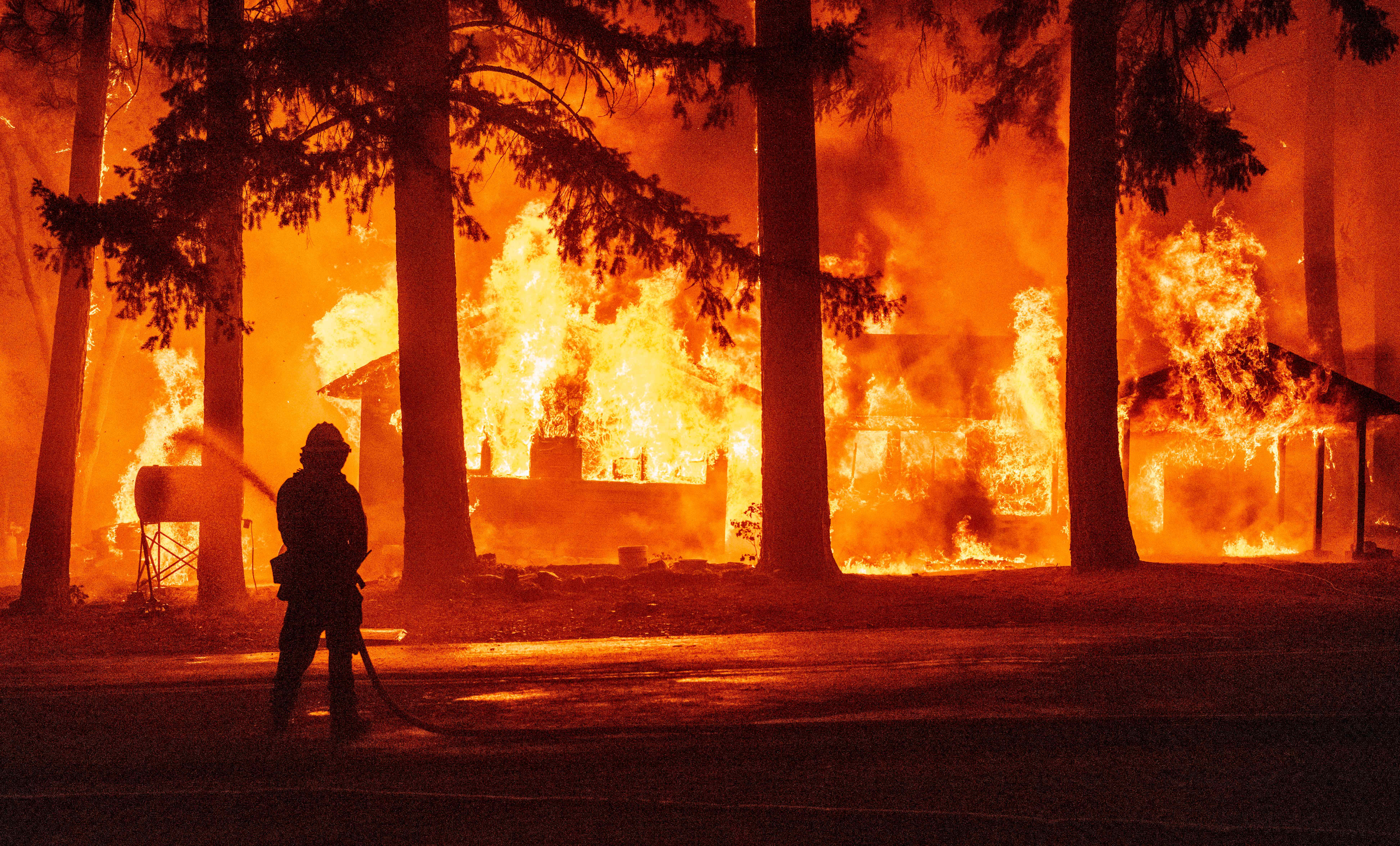 A firefighter sprays water on a propane tank as a home burns due to the Dixie fire in California