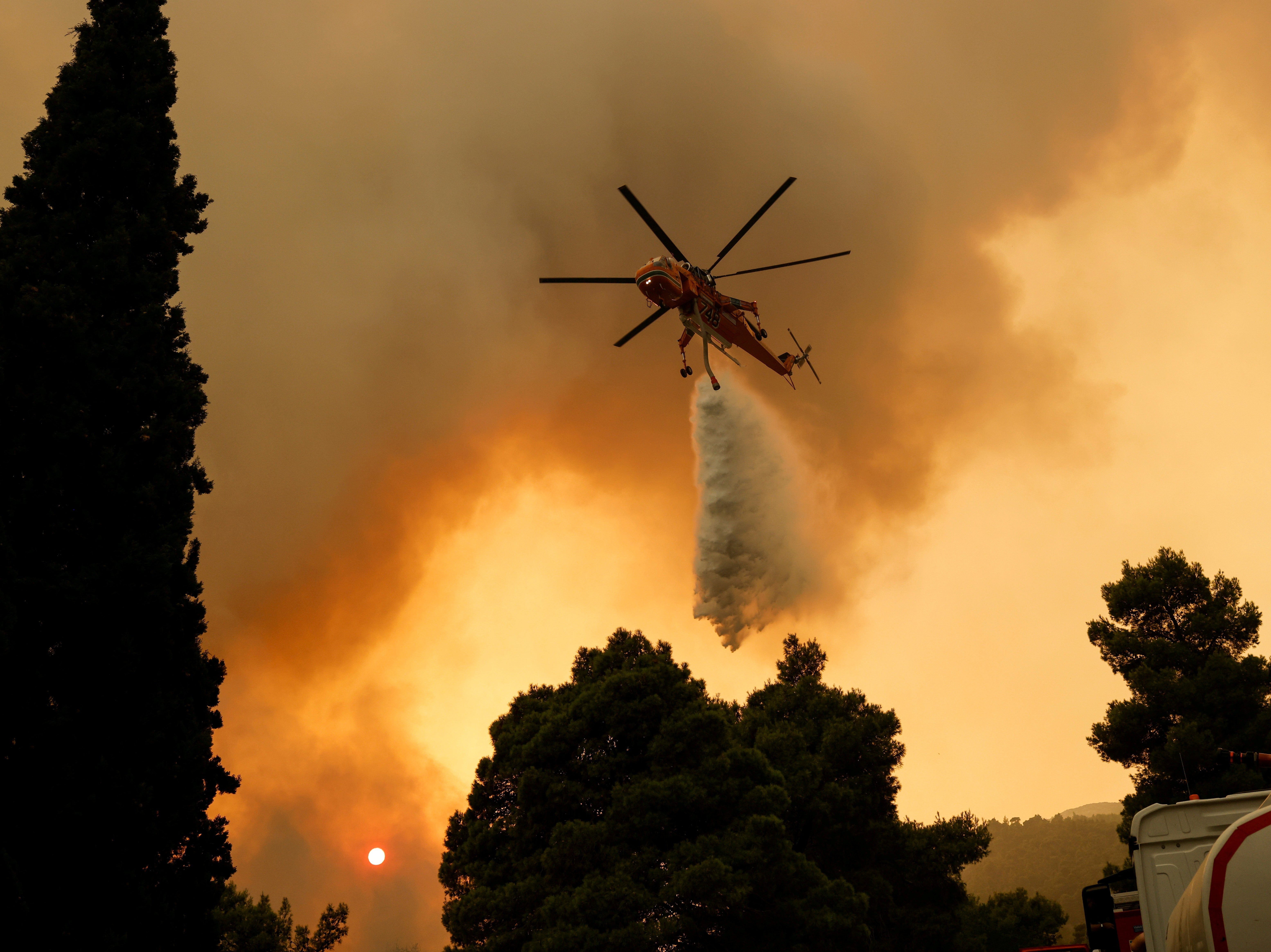 A firefighting helicopter makes a water drop as a wildfire burns in the village of Vilia, near Athens