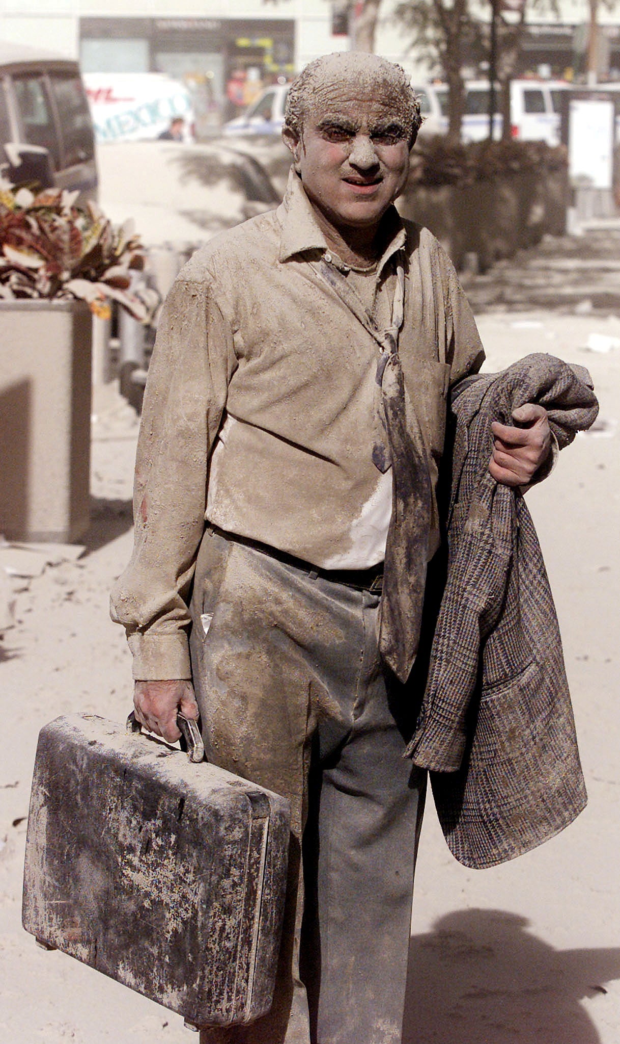 A man covered in dust walks in the street near the World Trade Center Towers