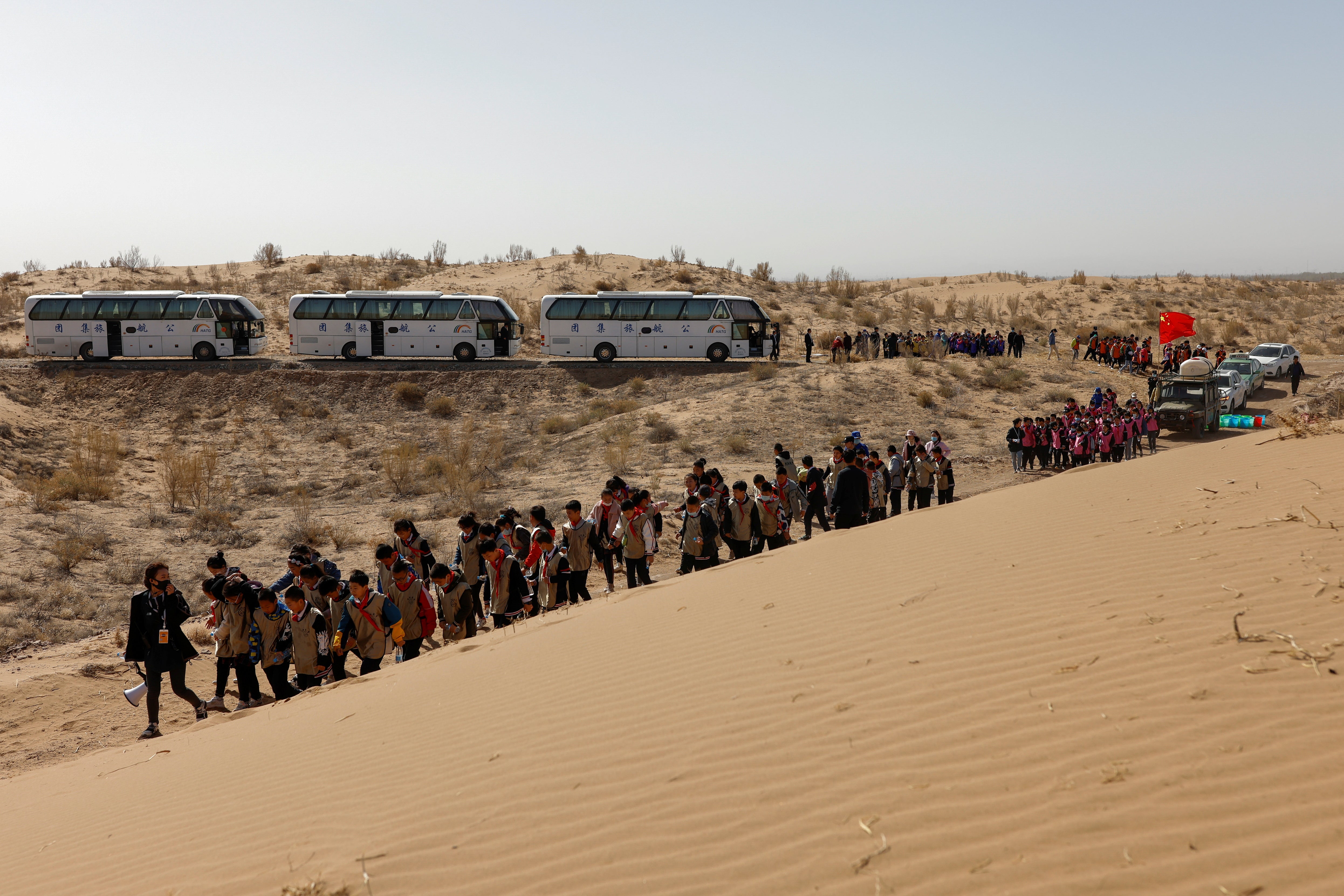 Children walk next to a sand dune during a voluntary tree-planting event organised by their school and the Wang family