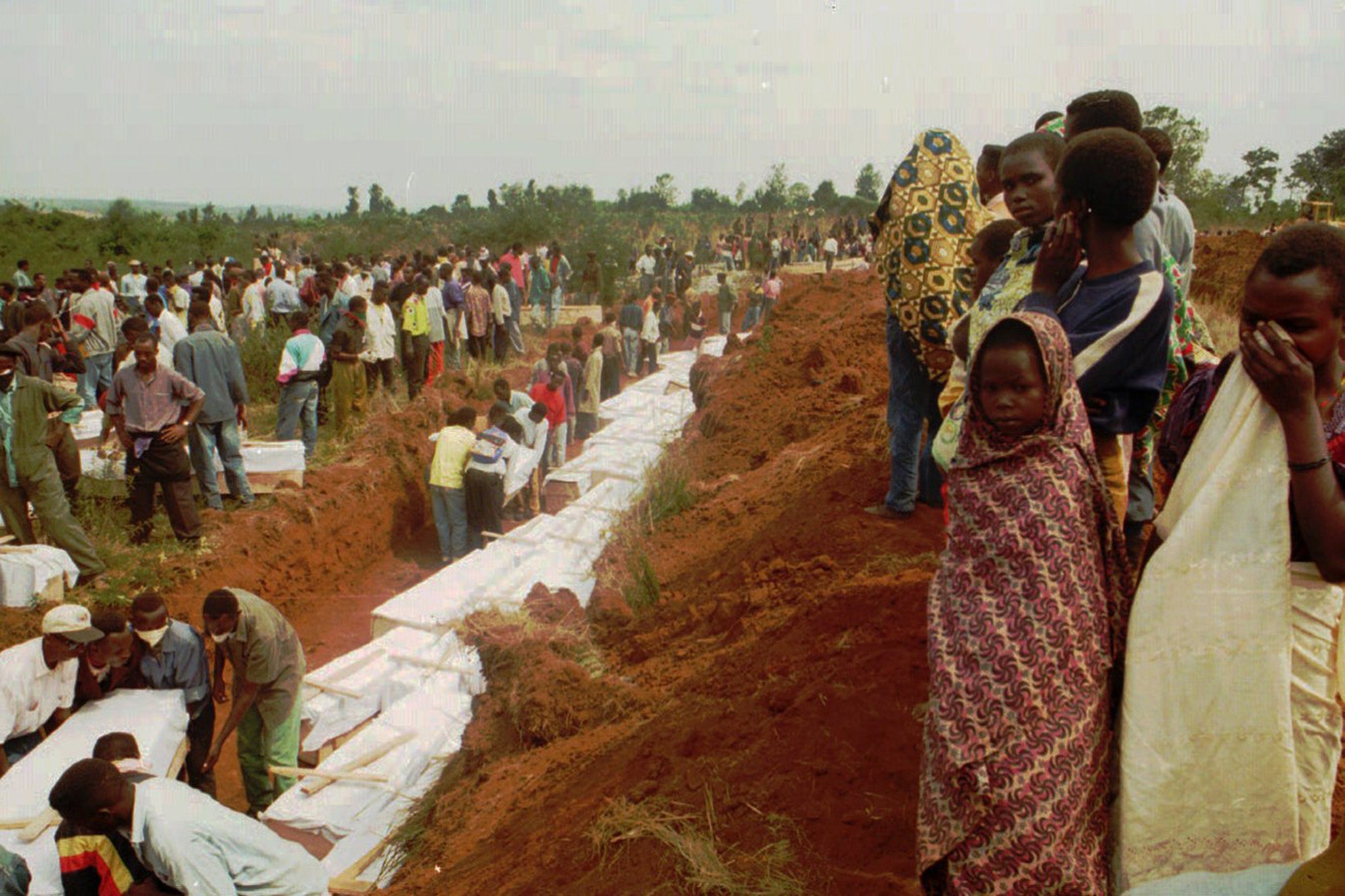 Survivors of a Hutu rebel attack on a displaced persons camp look on as the 320 victims, mostly women and children, are laid in a mass grave in Bugendena in 1996