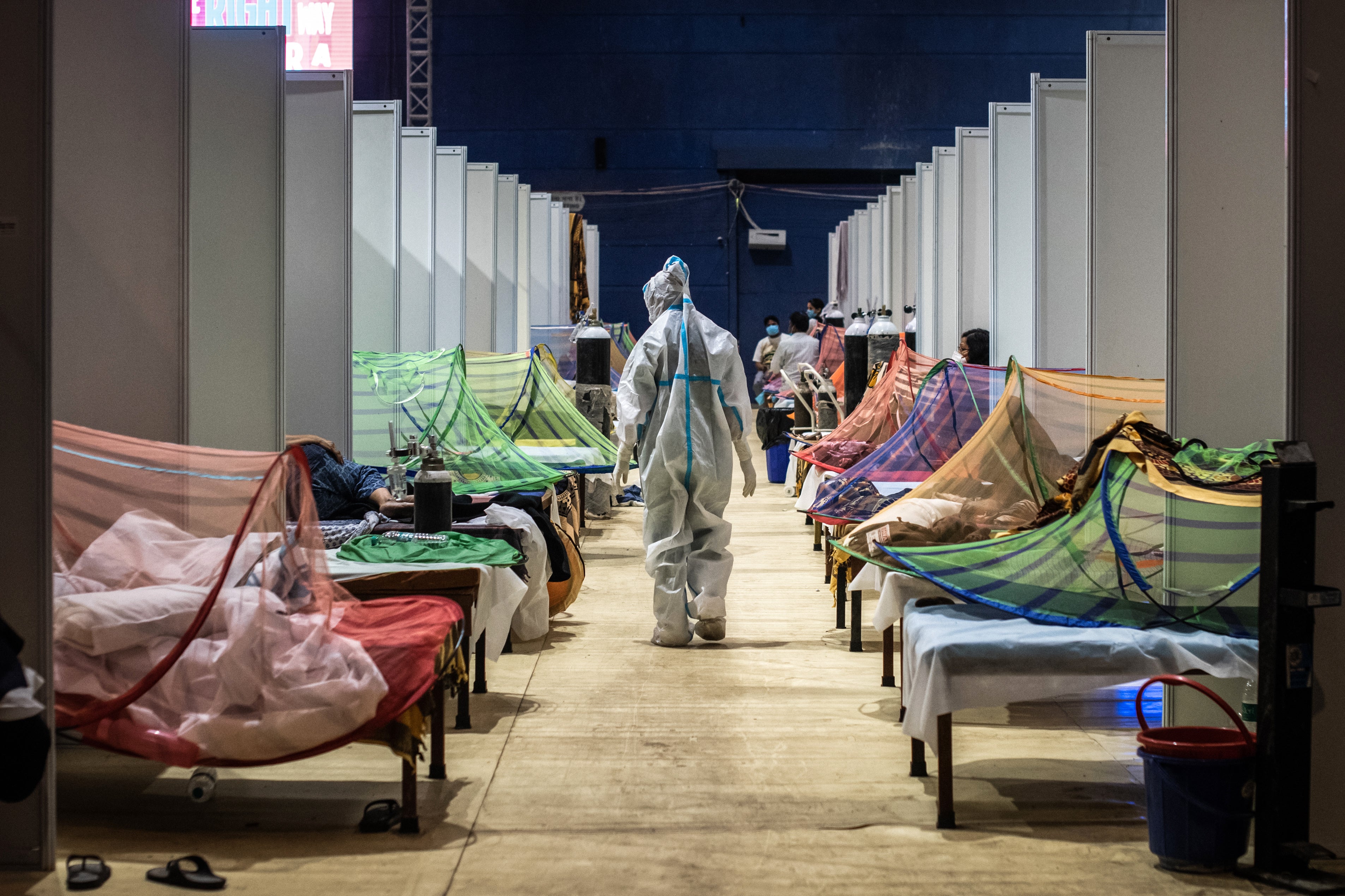 A medical worker in PPE observes Covid-19 patients inside a makeshift care facility in a sports stadium at the Commonwealth Games Village in Delhi