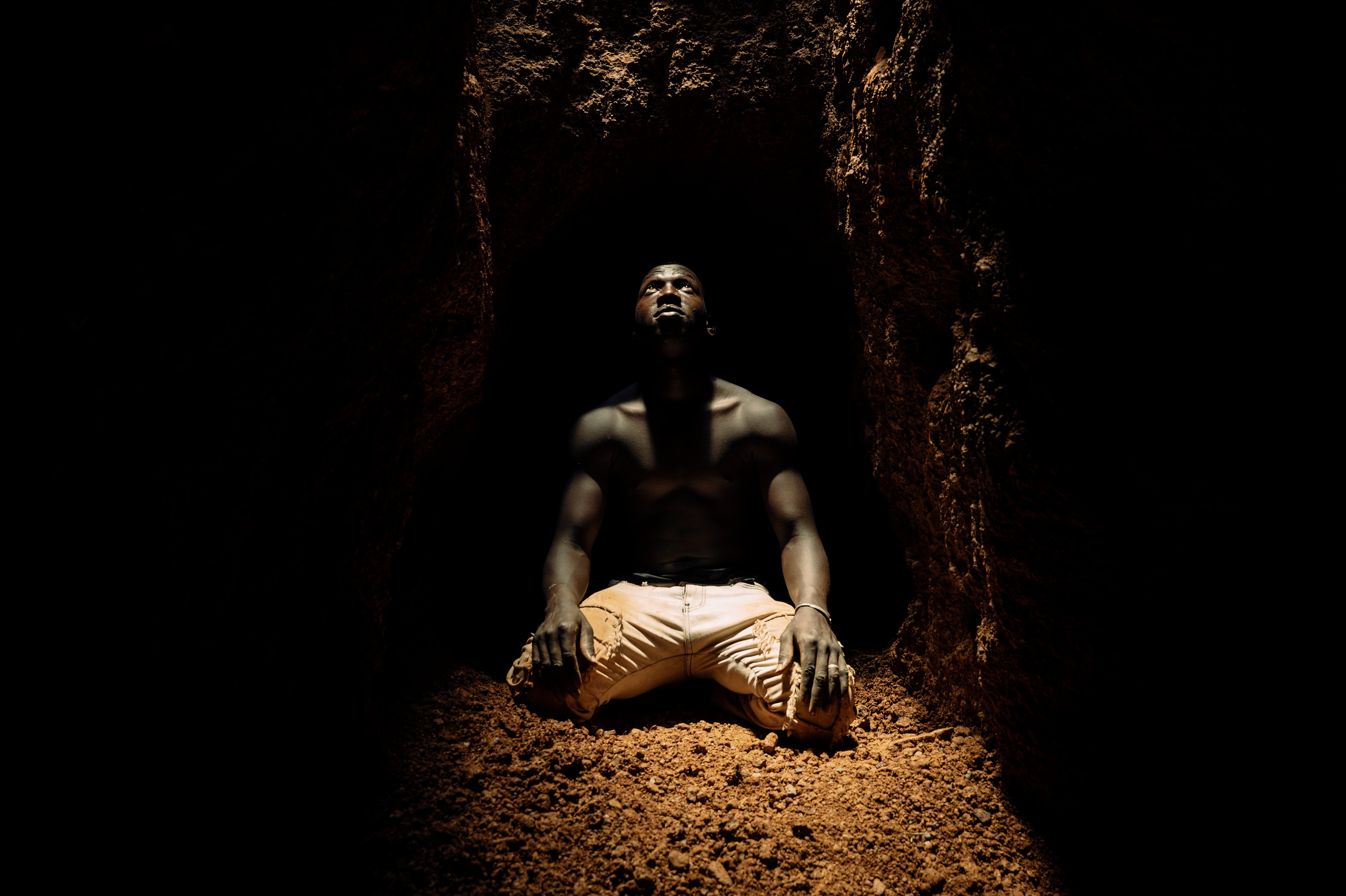 A miner kneeling at the bottom of a deep shaft catches his glimpse of daylight before retreating along a tunnel which extends as far as 200 metres