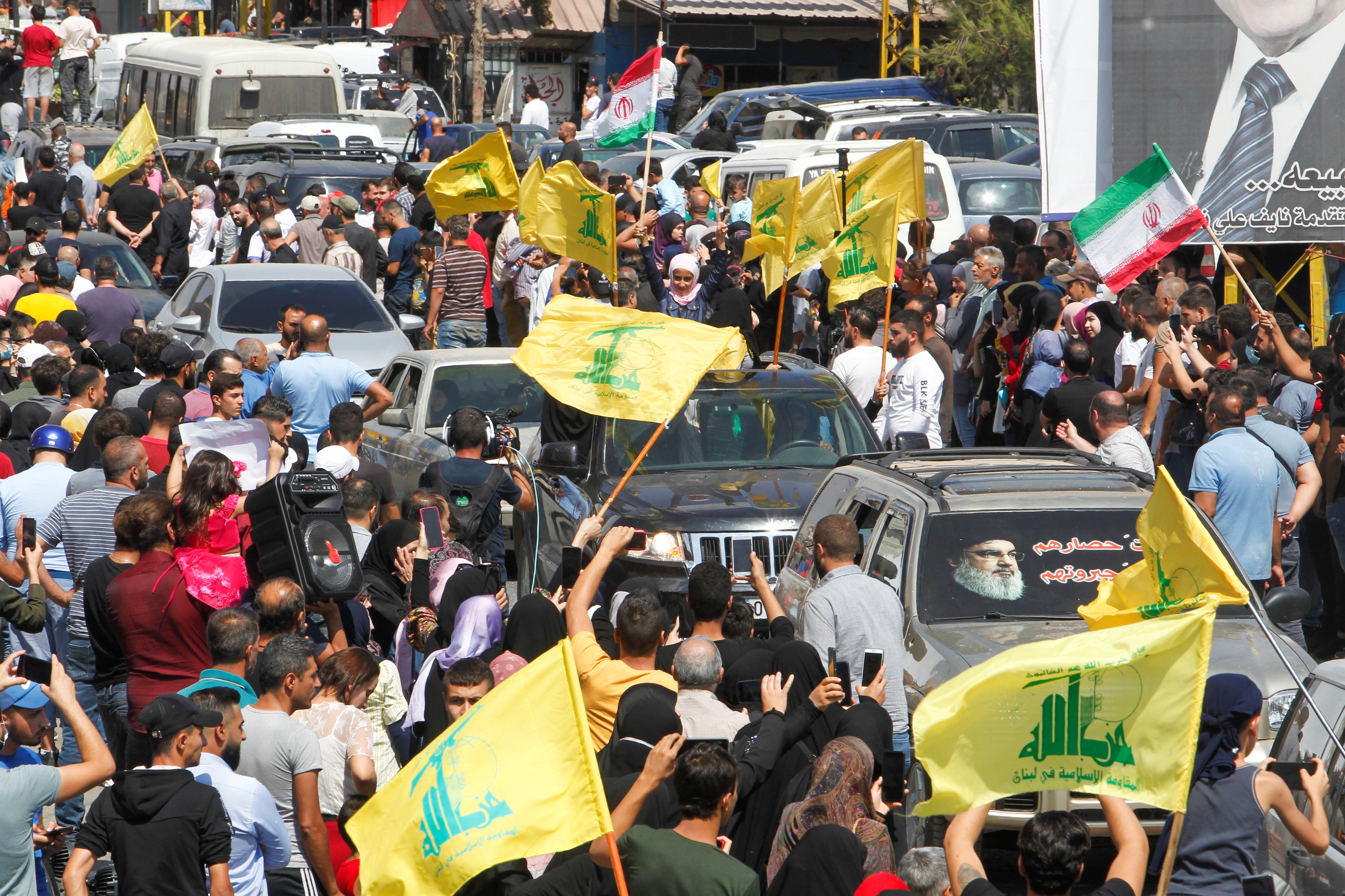 People wave Hezbollah and Iranian flags as a convoy of tanker trucks carrying Iranian fuel drives through the streets