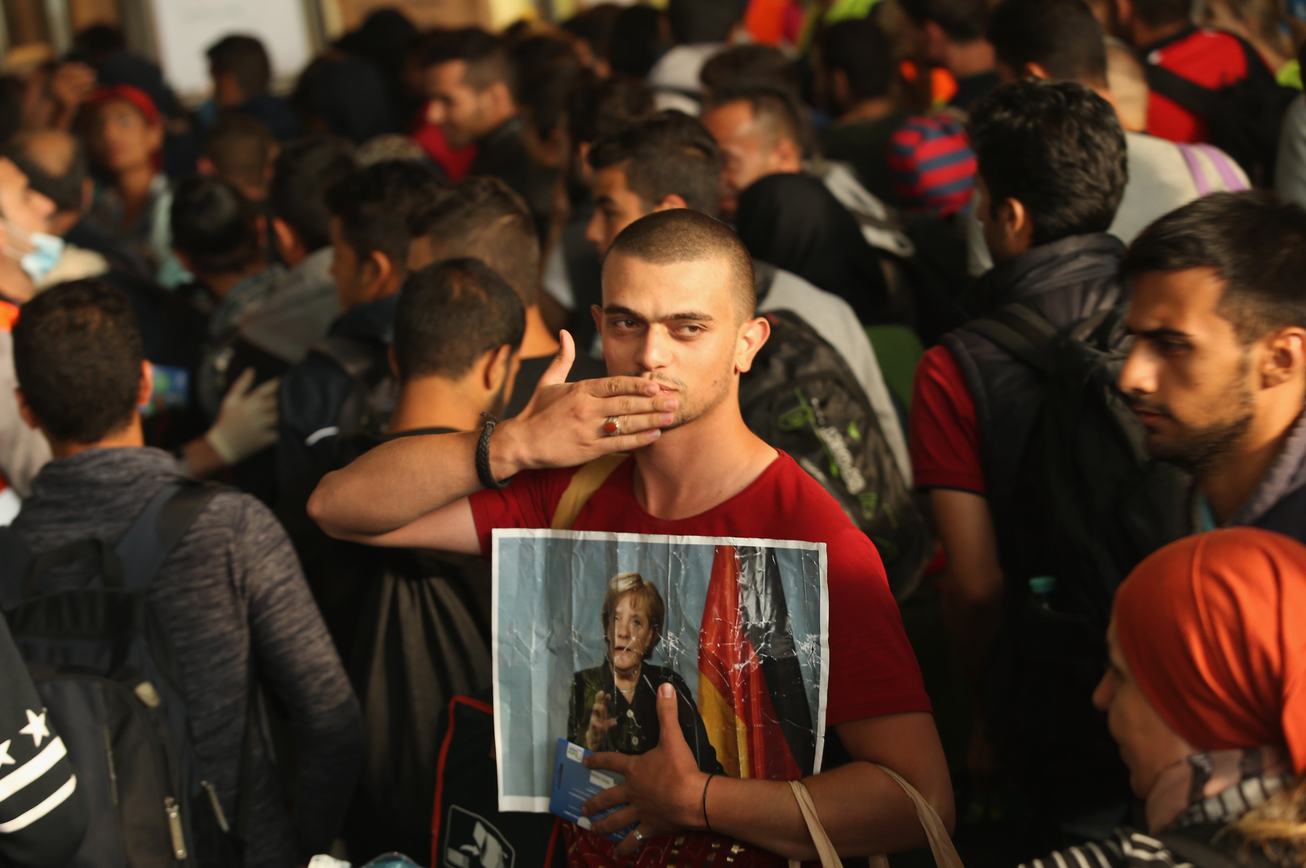 A migrant from Syria holds a picture of Merkel as he and 800 others arrive from Hungary in 2015