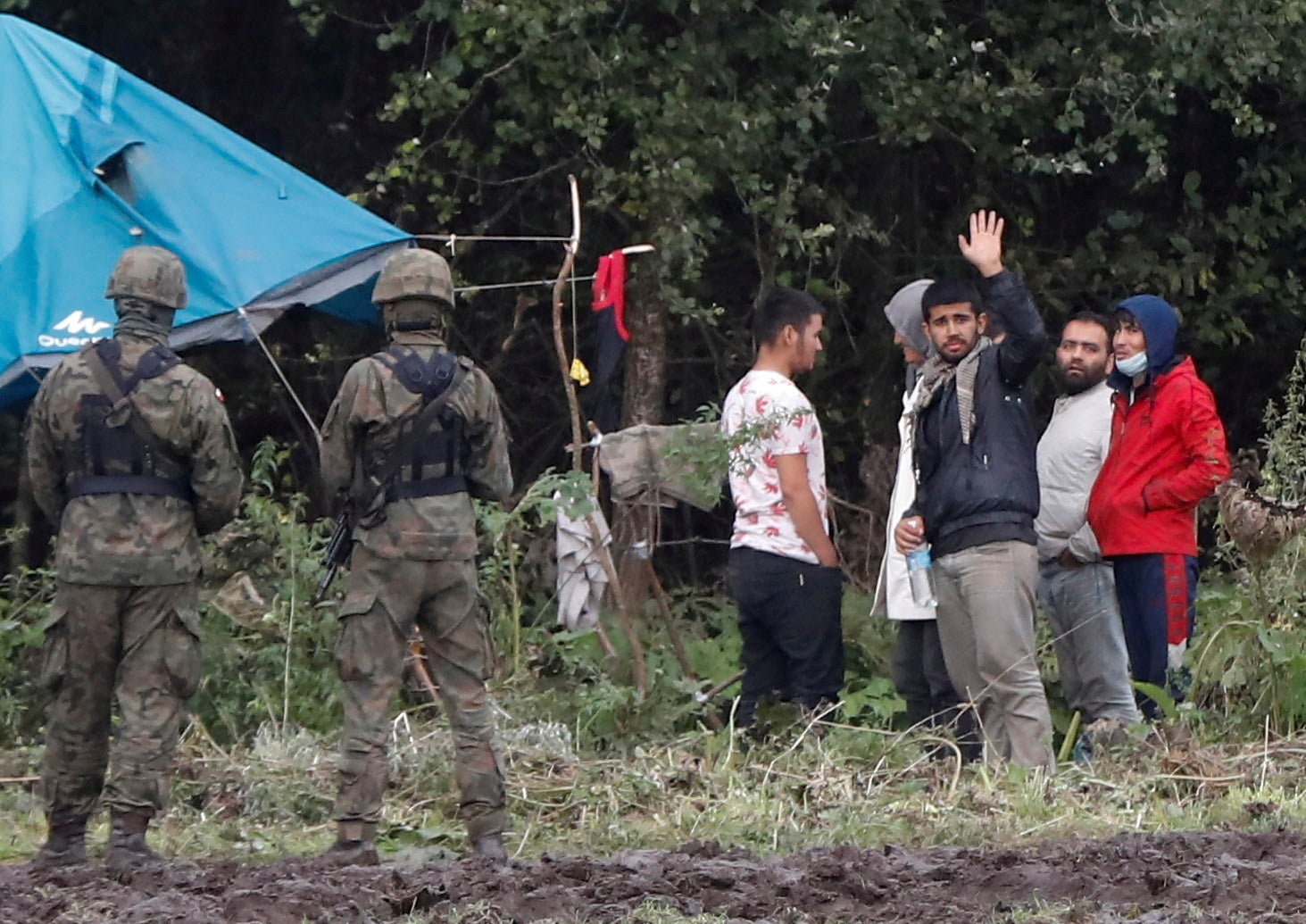 Polish border guard officers stand guard next to a group of migrants stranded on the border between Belarus and Poland