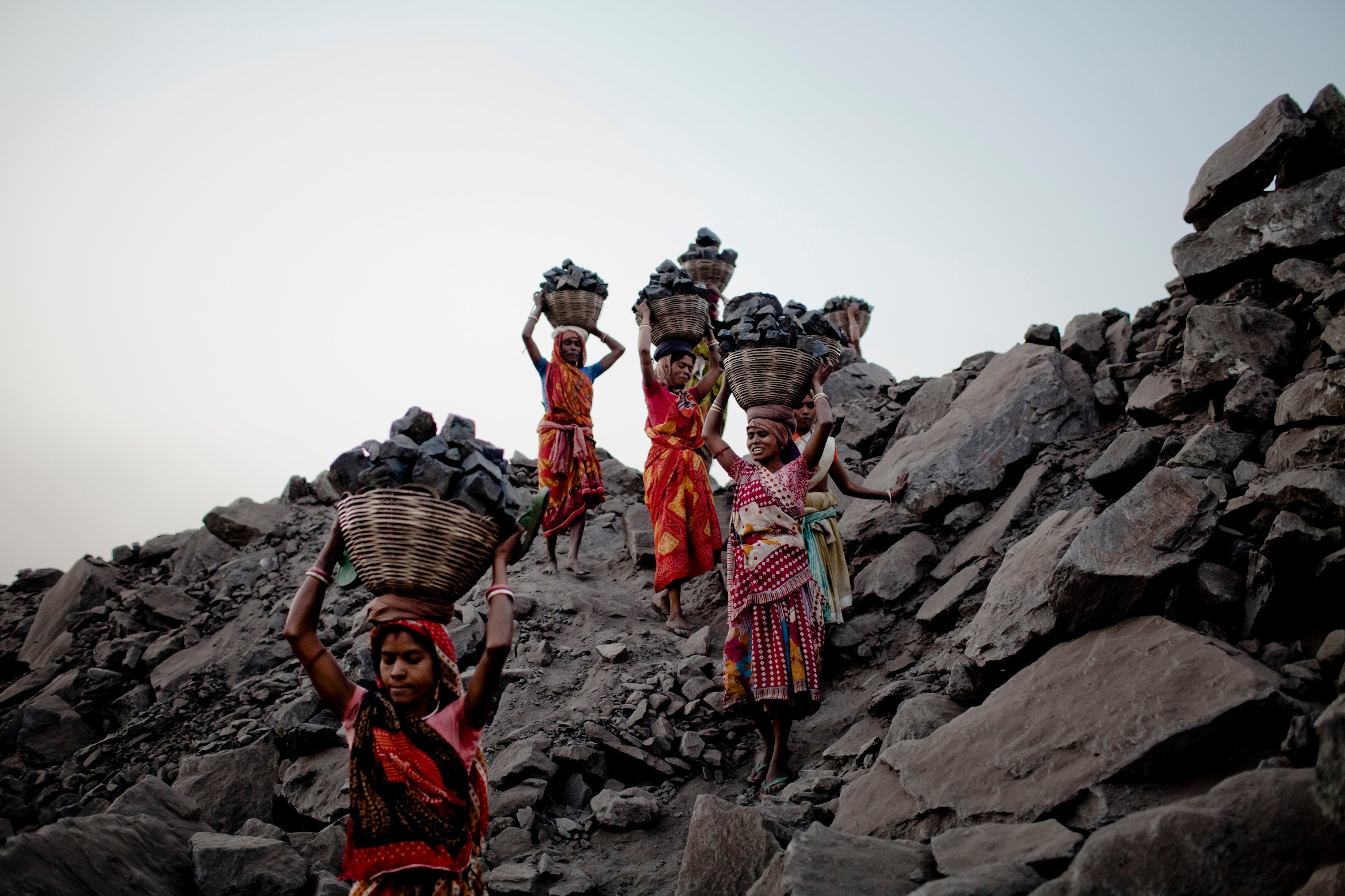 Women scavenge coal illegally from an open-cast mine and carry it back to their village for sale