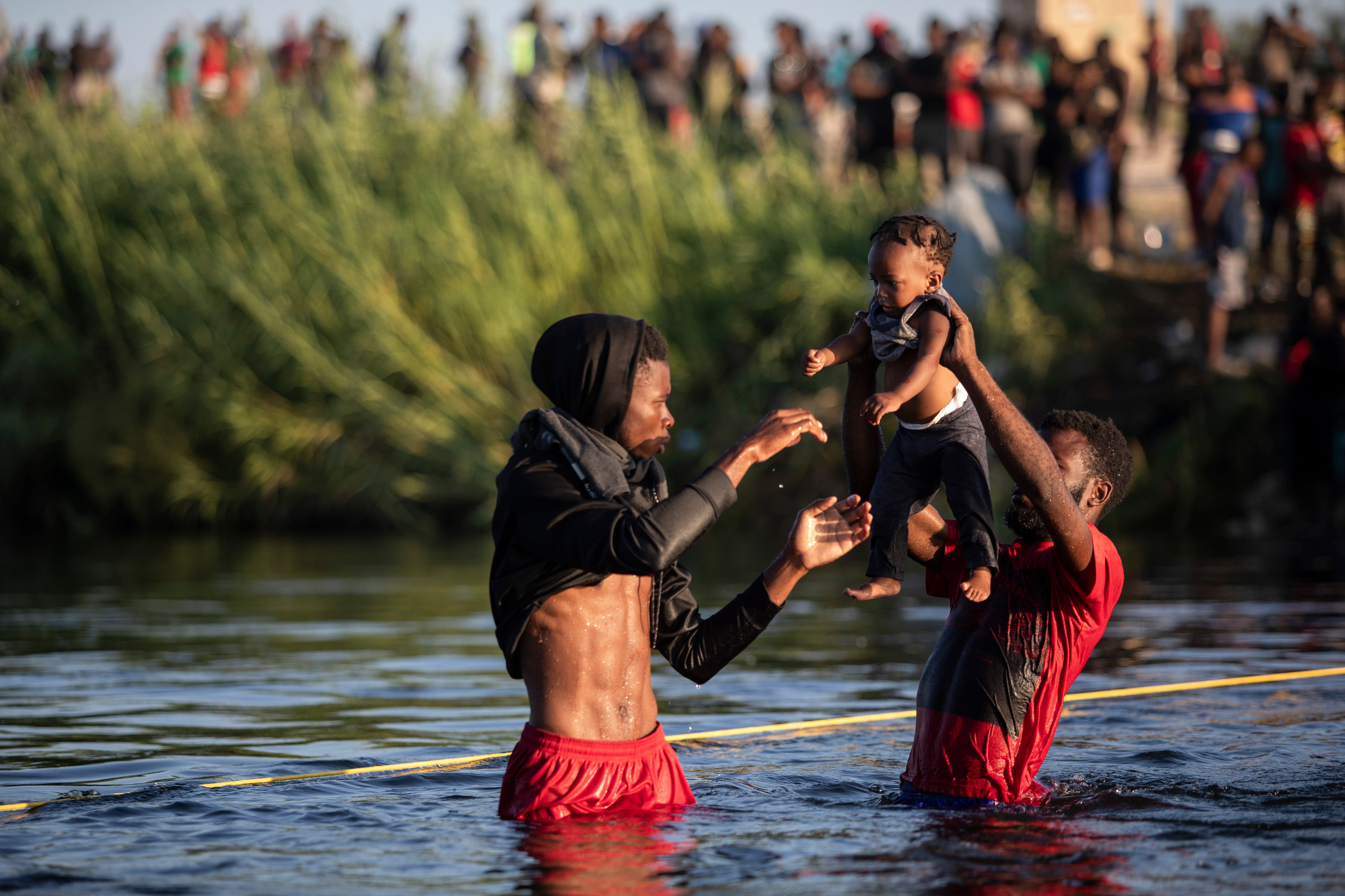 Men lift a baby over the waters of the Rio Grande river as migrants, many from Haiti, wade across the from Del Rio, Texas, to return to Ciudad AcuÃ±a, Mexico, Monday, 20 September 2021, to avoid deportation from the US