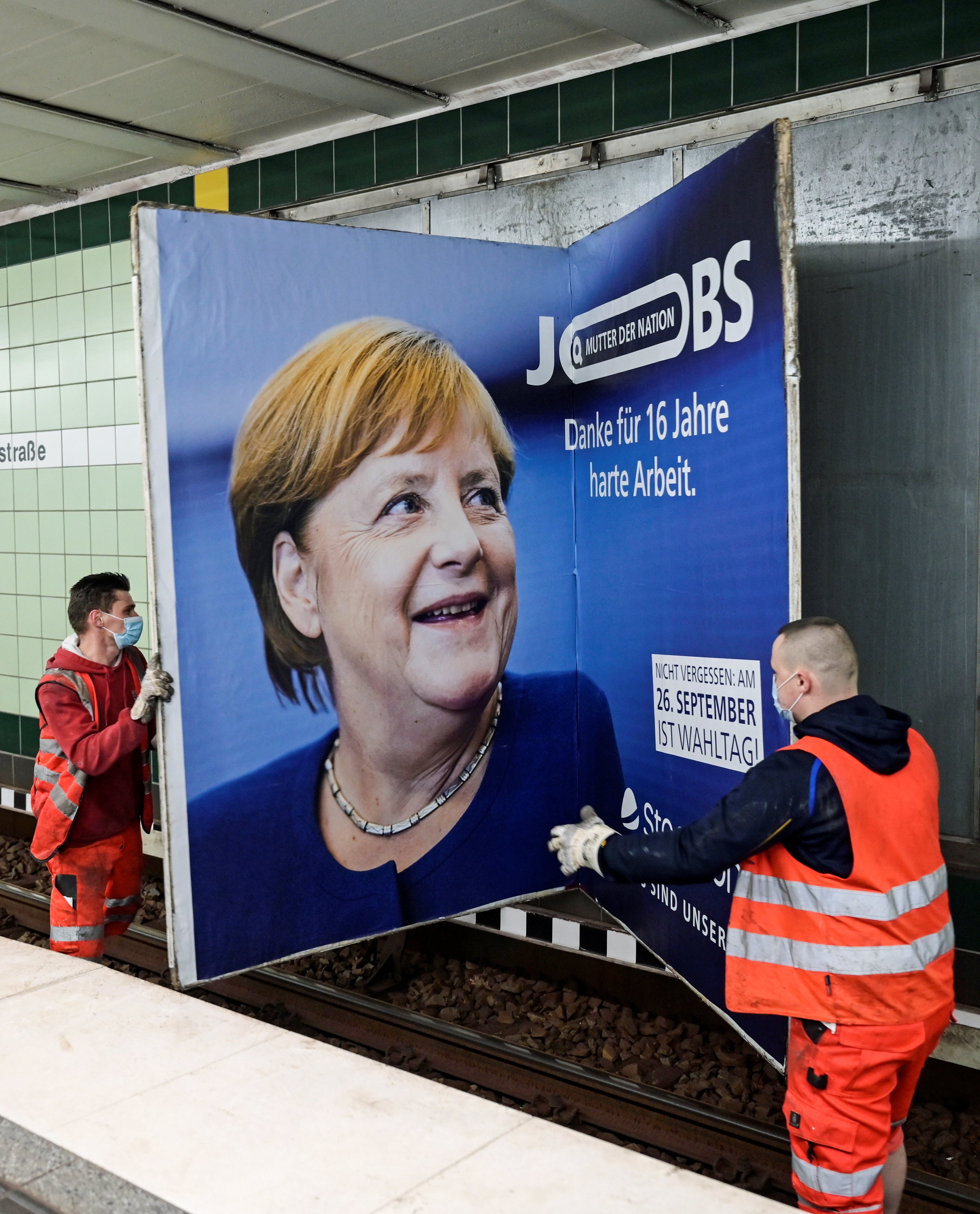 Workers remove an advertisement showing German Chancellor Angela Merkel with a slogan that reads ‘Mother of Nation: Thanks For 16 Years of Hard Work’