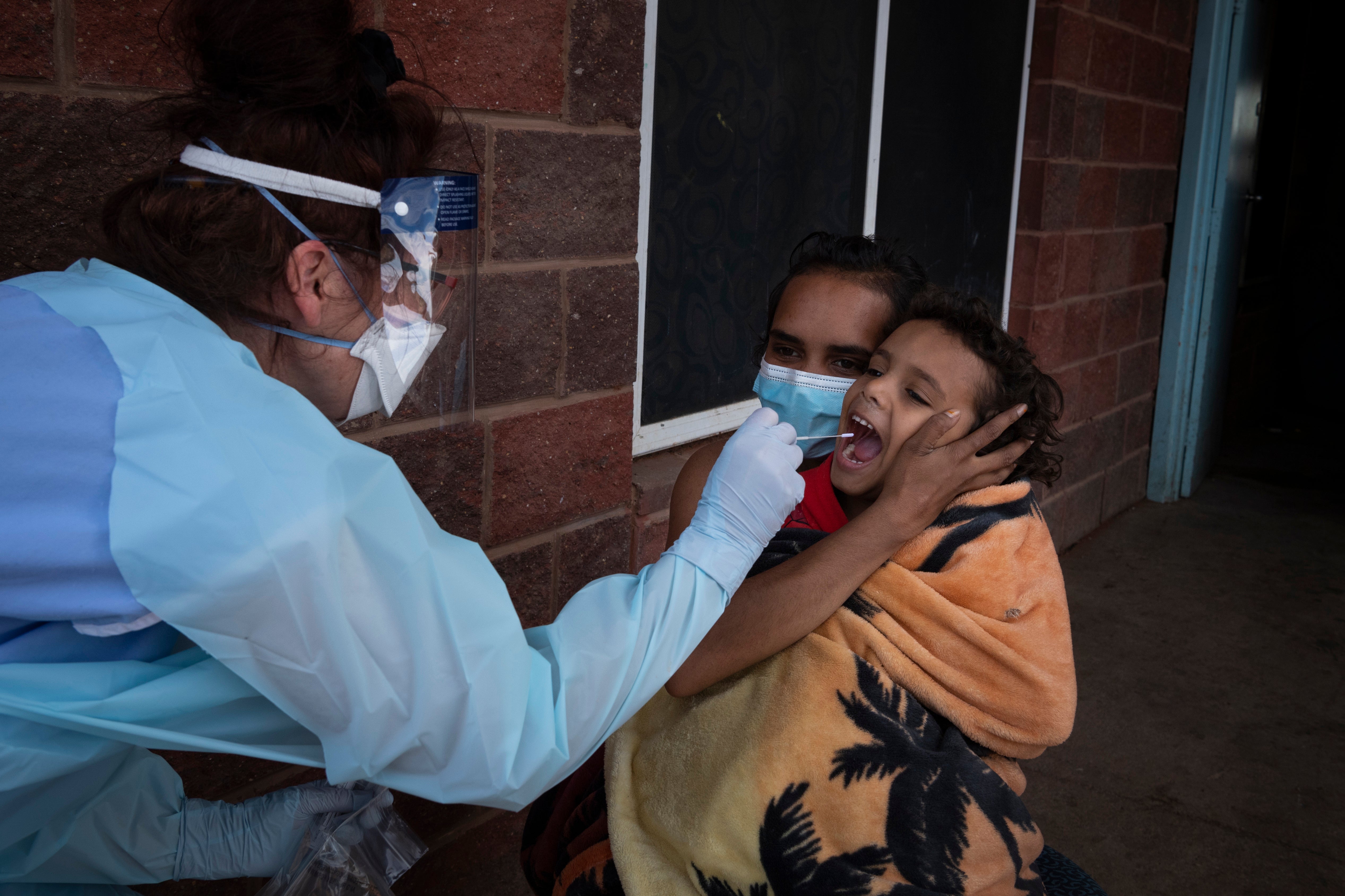 Brooke Johnson holds her son Christopher while a New South Wales Health worker takes a Covid swab