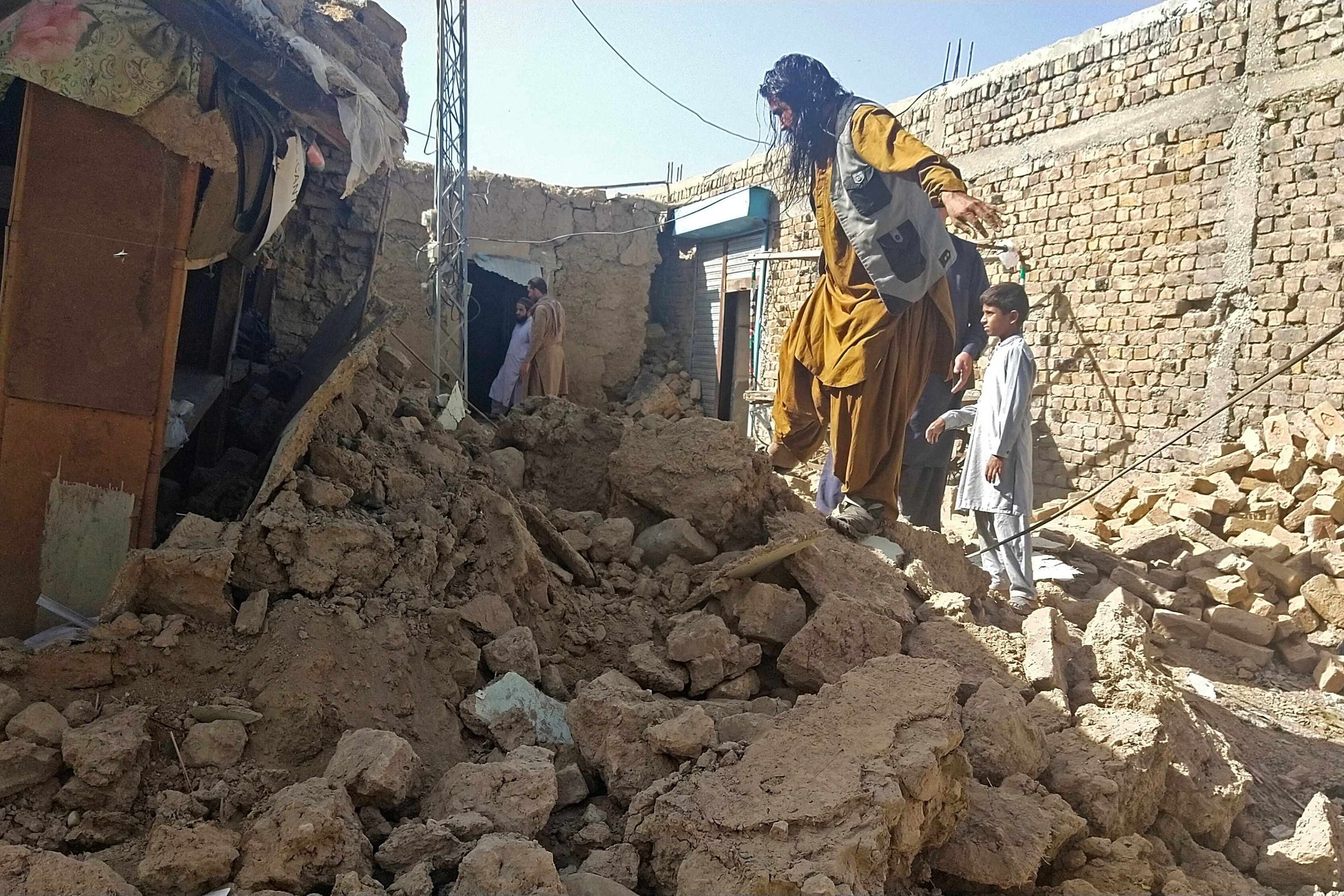 Residents gather next to the wreckage of their home, which collapsed following an earthquake in the remote mountainous district of Harnai, Pakistan