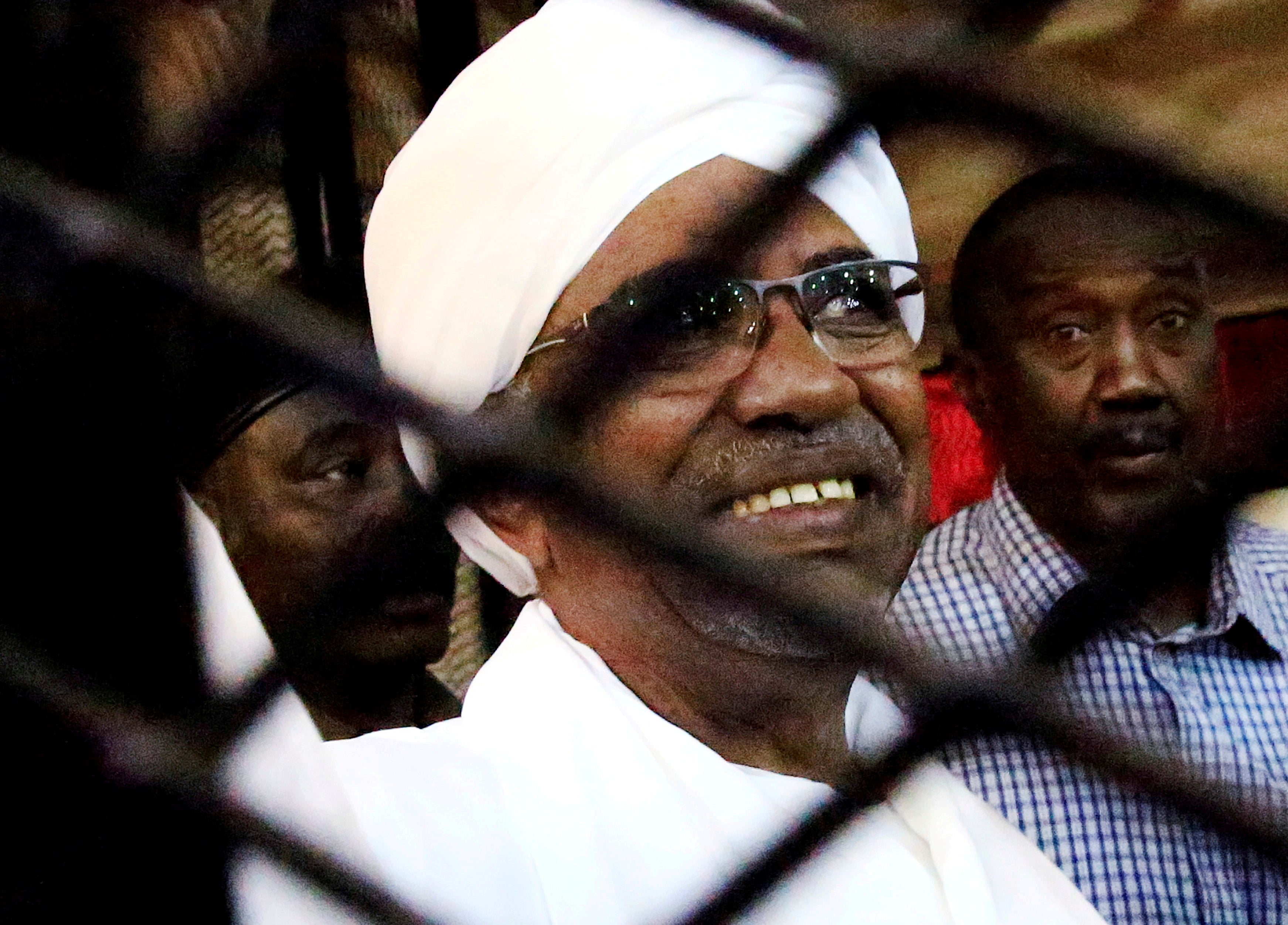 Sudan's former president Omar Hassan al-Bashir smiles as he is seen inside a cage at the courthouse where he is facing corruption charges, in Khartoum