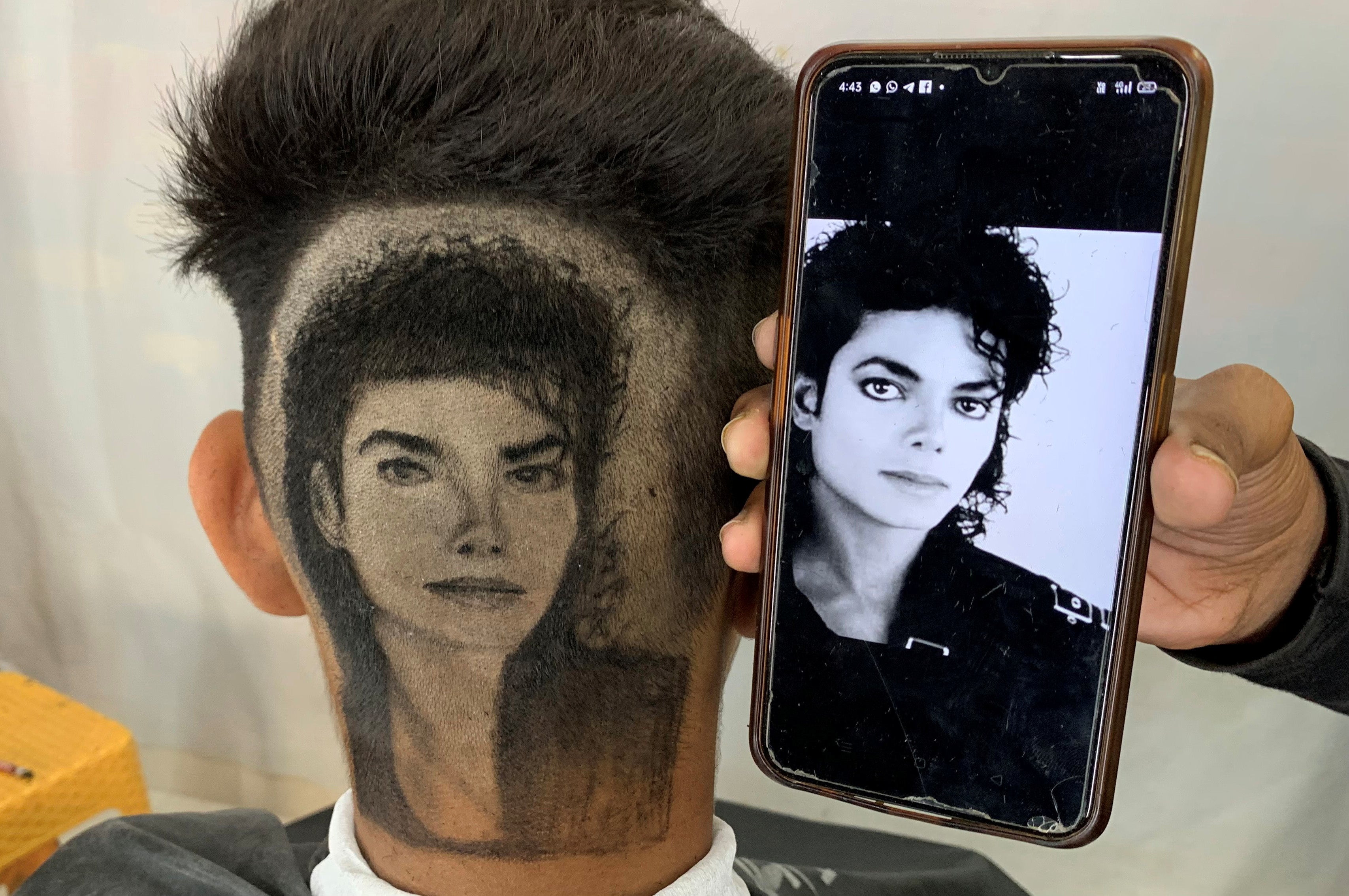 Gurwinder Singh Sidhu displays a photo of Michael Jackson next to a customer after he made a hair tattoo of the pop star in the customer's hair inside his shop in Dabwali town