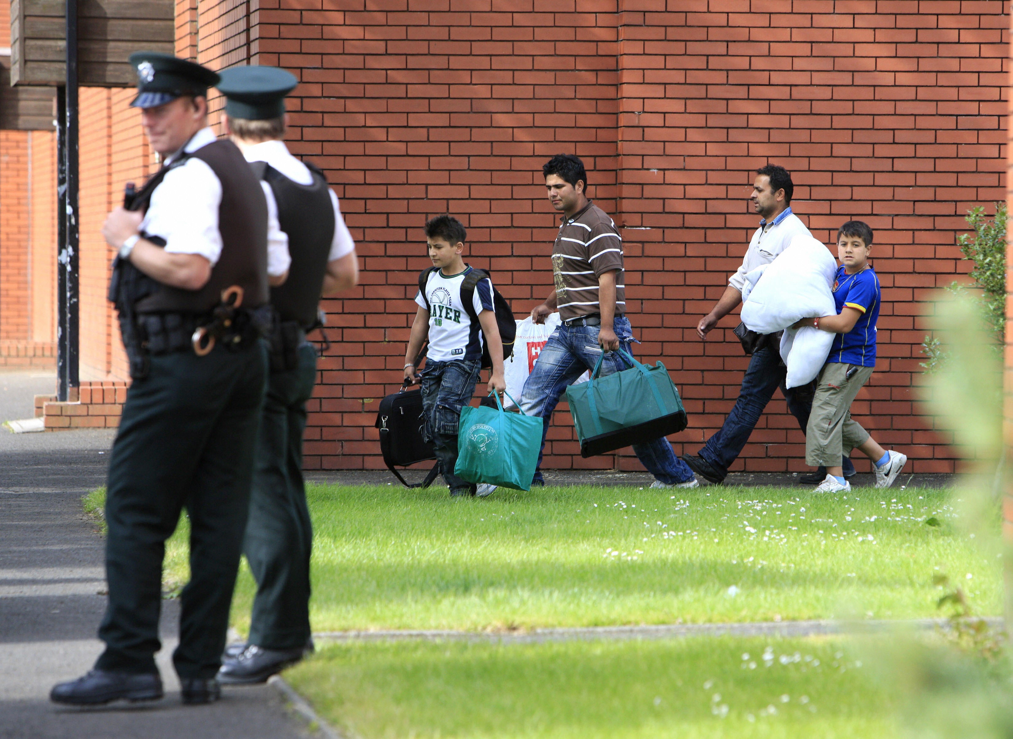 Romanian families leave a leisure centre in Belfast under police protection. More than 100 Romanian people were forced to flee their homes after racist attacks