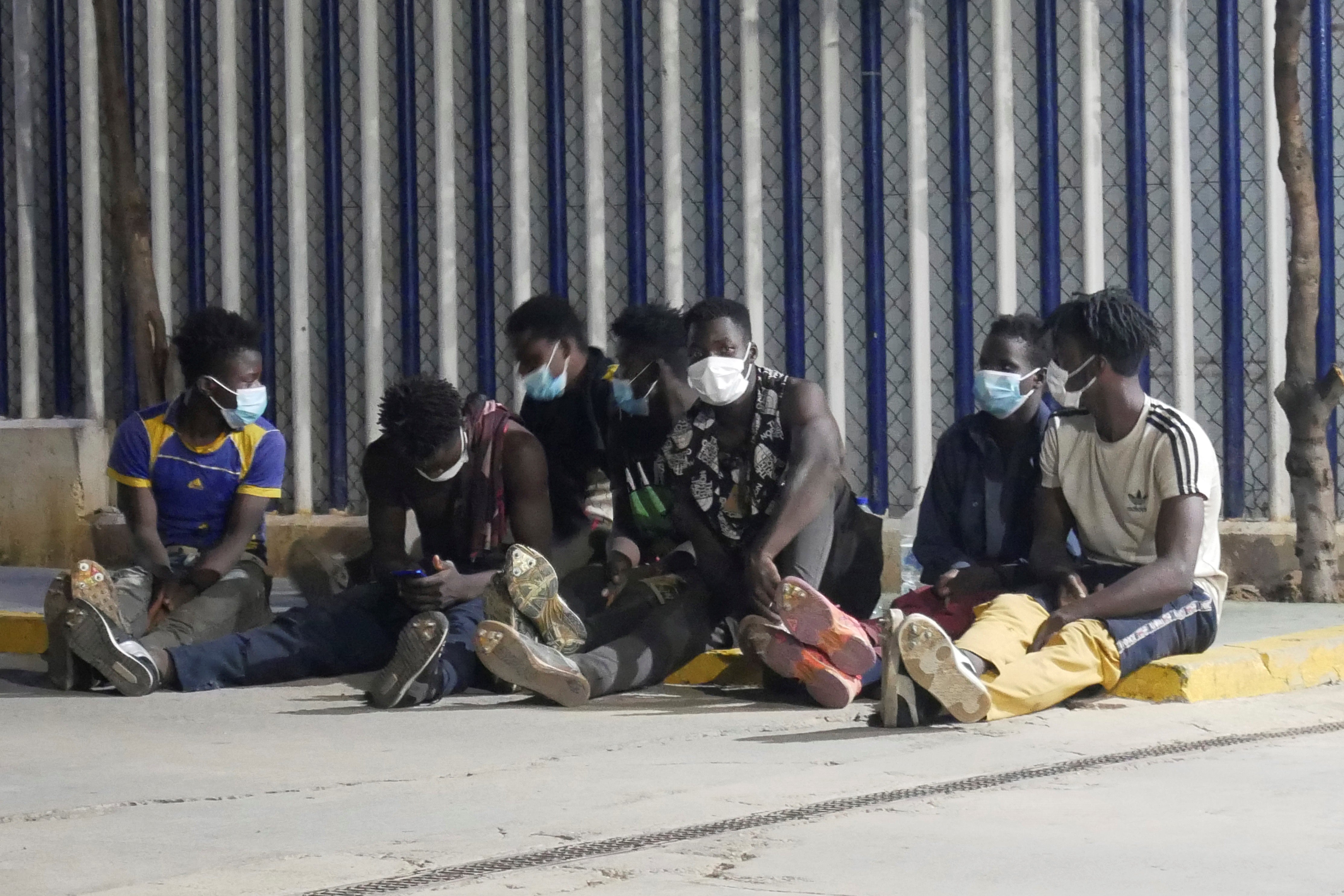 Several migrants wait next to several policemen after they managed to jump the border fence to reach the Spanish enclave of Melilla from neighbouring Morocco