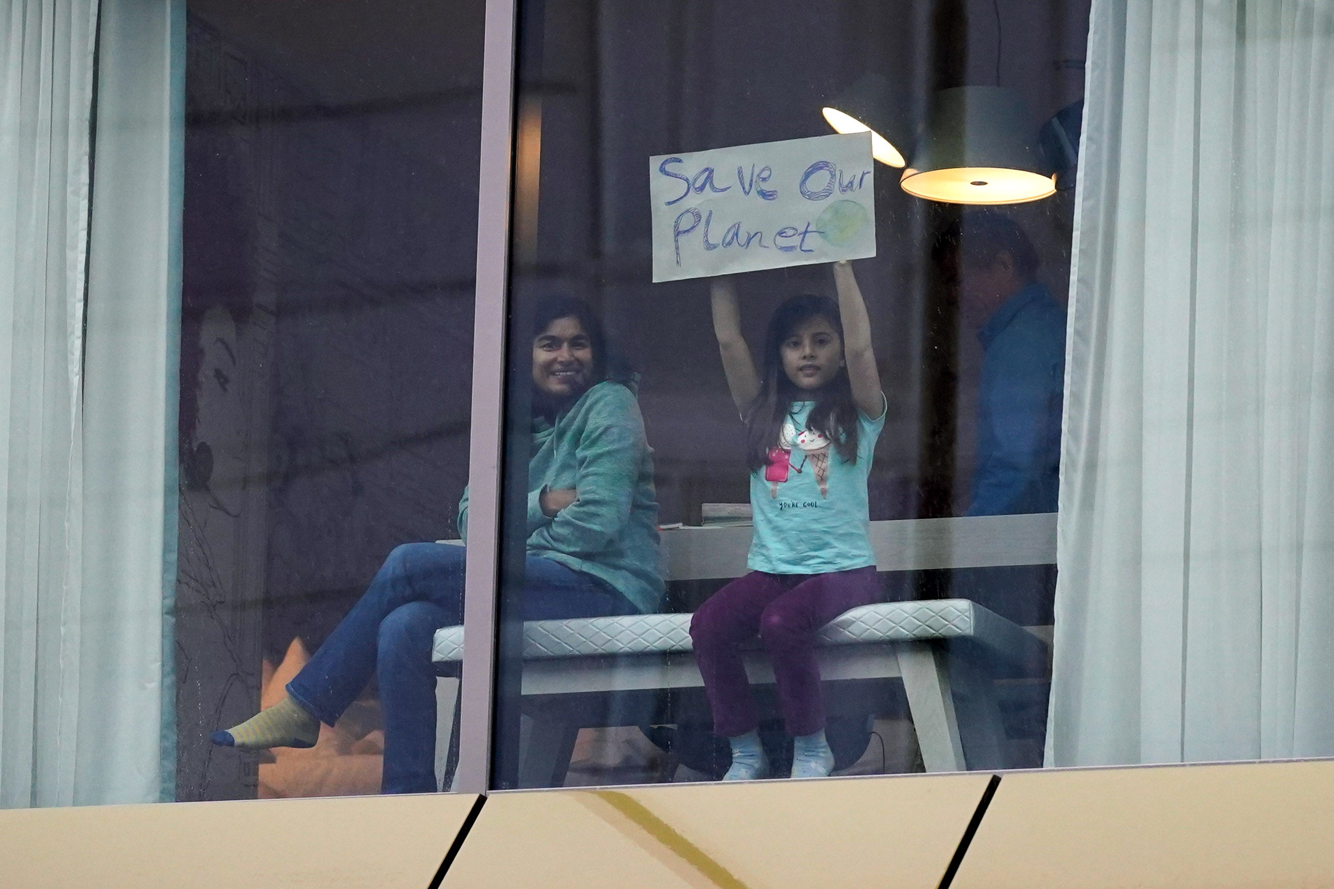 A young girl holds up a sign saying ‘save our planet’ at a hotel window overlooking the conference