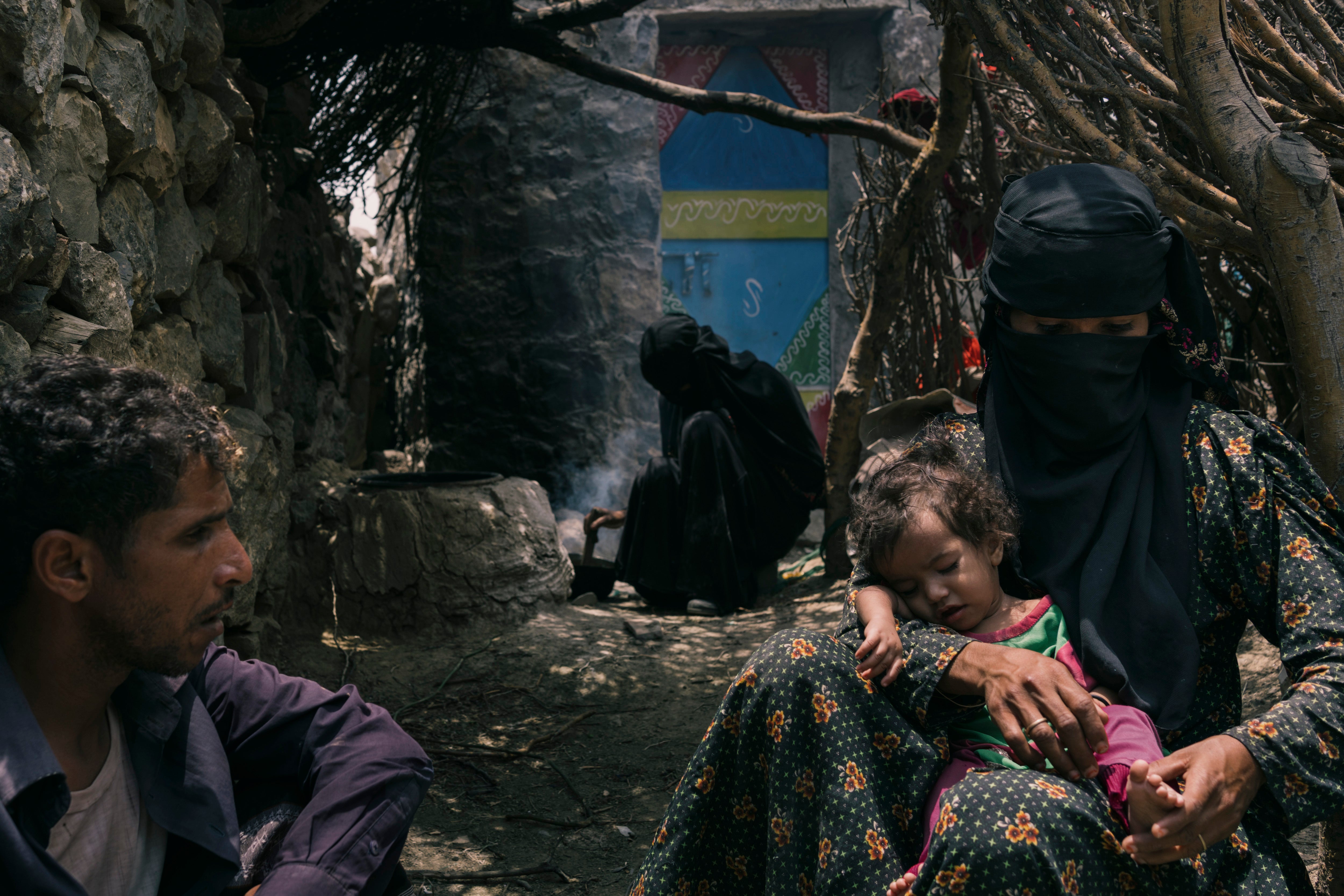 Bushra holds her daughter outside their home with her husband