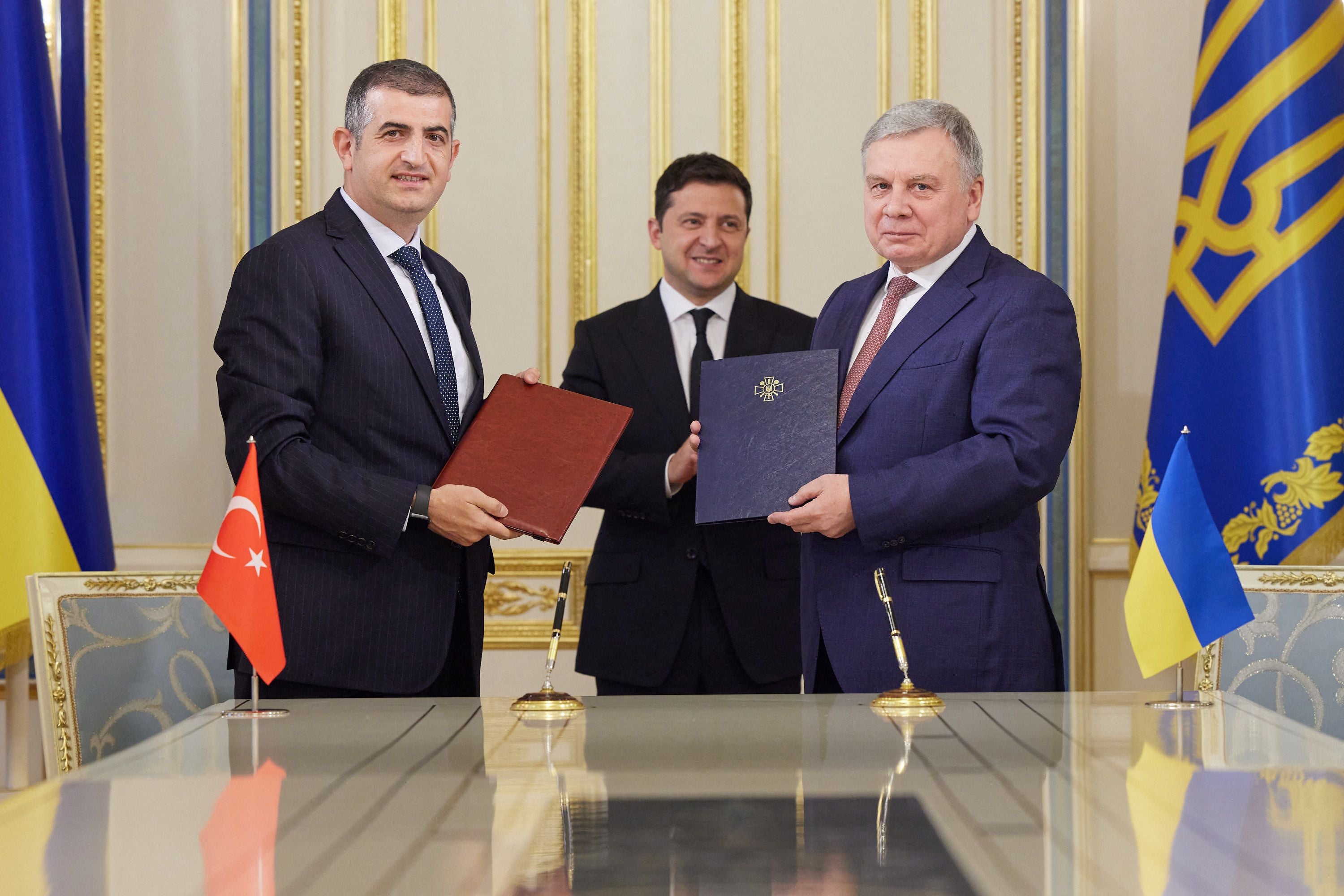 Ukrainian President Volodymyr Zelensky (C) next to Ukraine's Defence Minister Andriy Taran (R) and Haluk Bayraktar, CEO of the Turkish drone magnate Baykar, as they hold folders with signed documents in Kiev