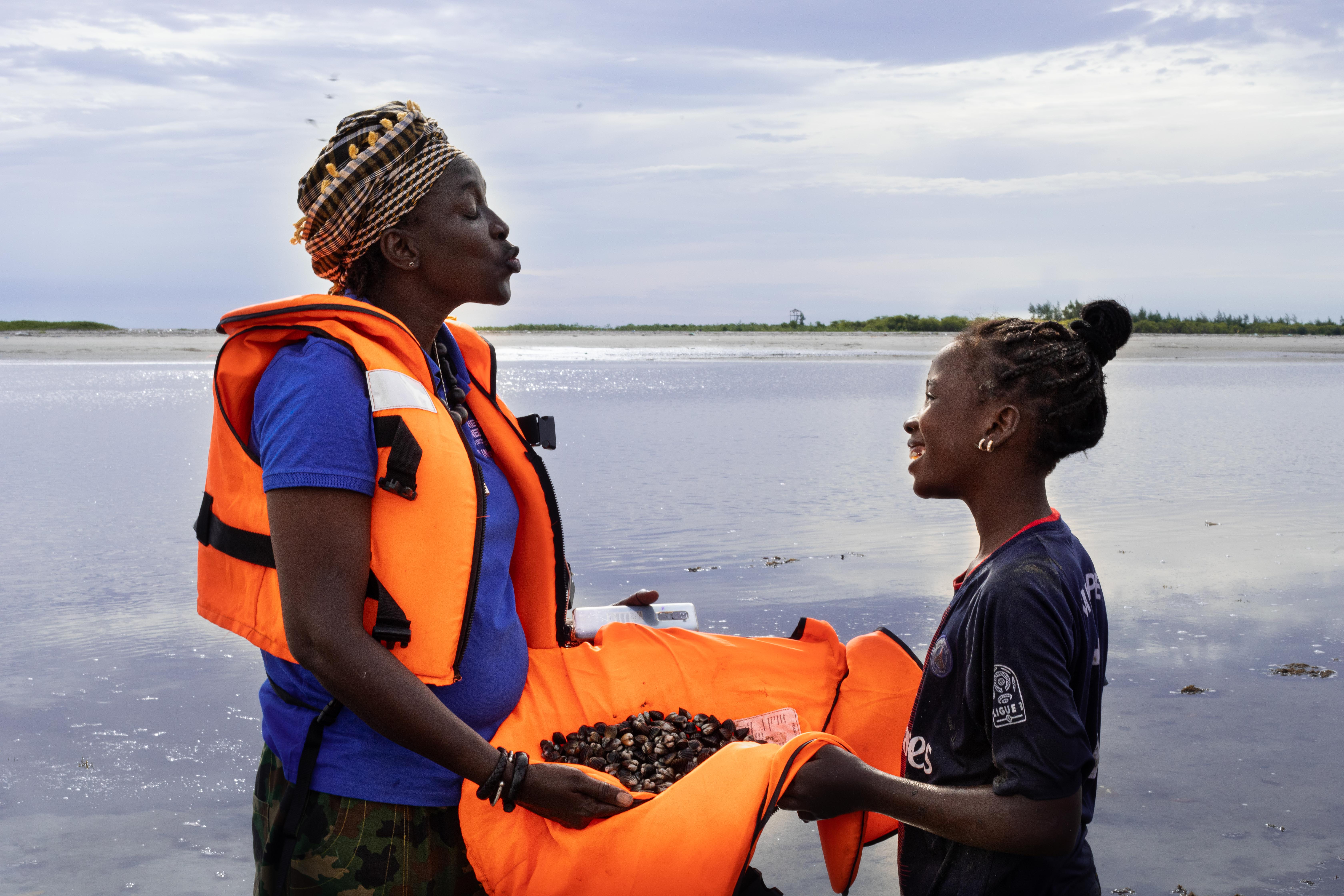 Coumba Dieng, an MSI team member with a young girl from a fishing community, holding cockles that they collected