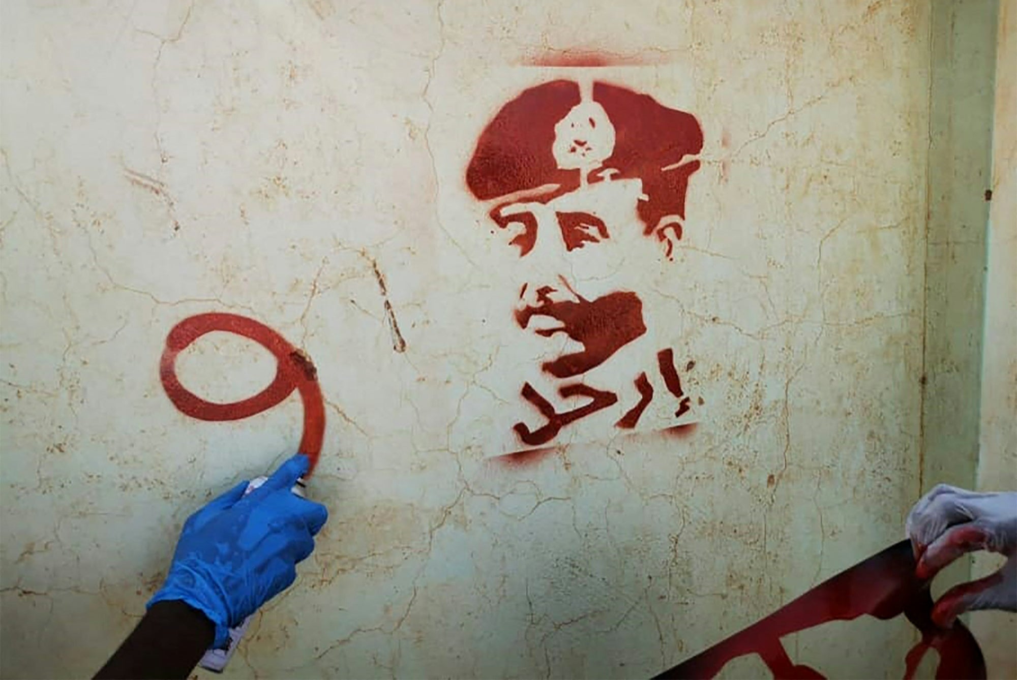 A Sudanese youth sprays paint next to a stencil painting of the country's top army general Abdel Fattah al-Burhan, with writing in Arabic that reads ‘leave’