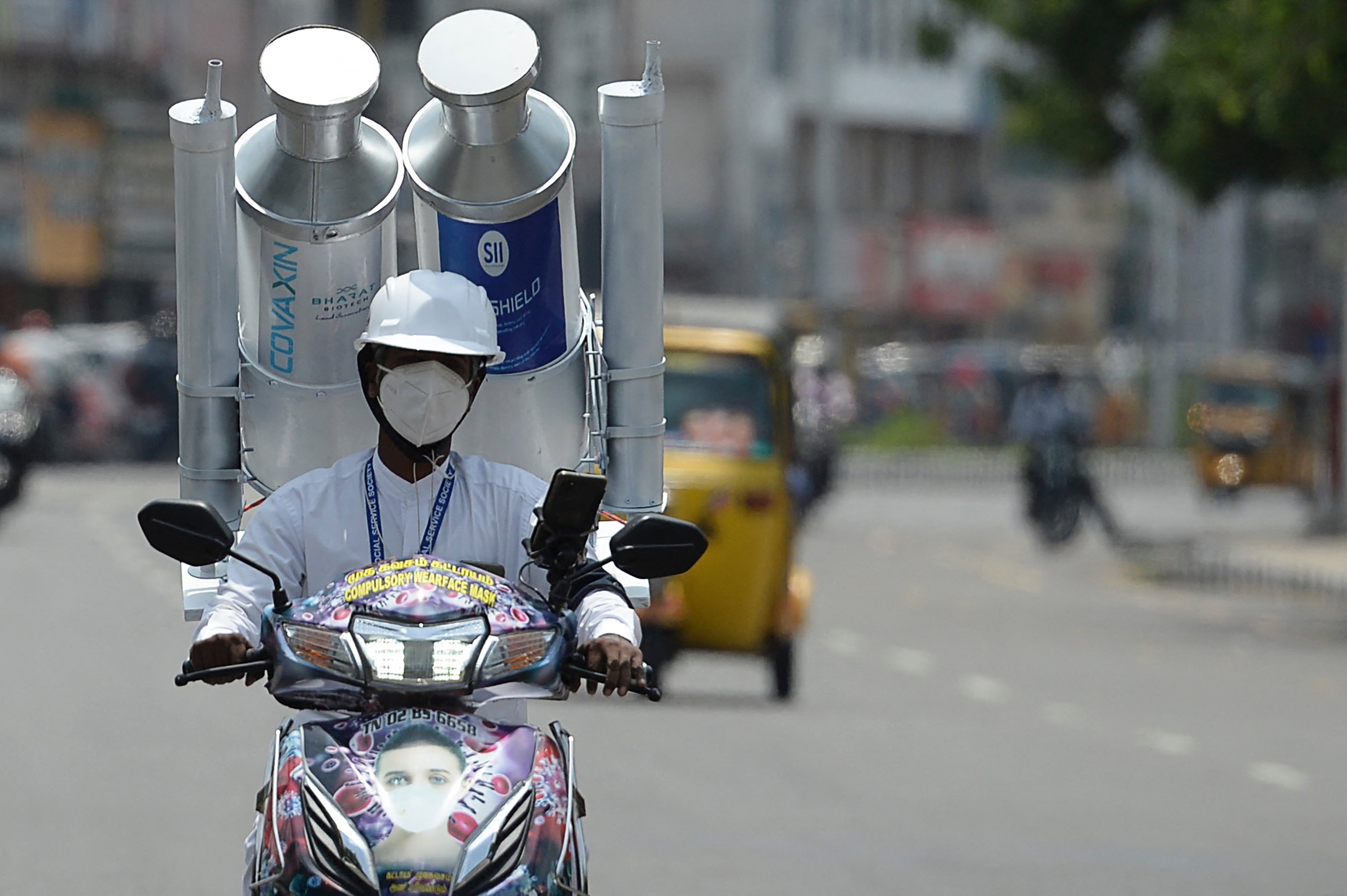 A volunteer rides along a road with a mock vials of India-made vaccine Covishield and Covaxin in India