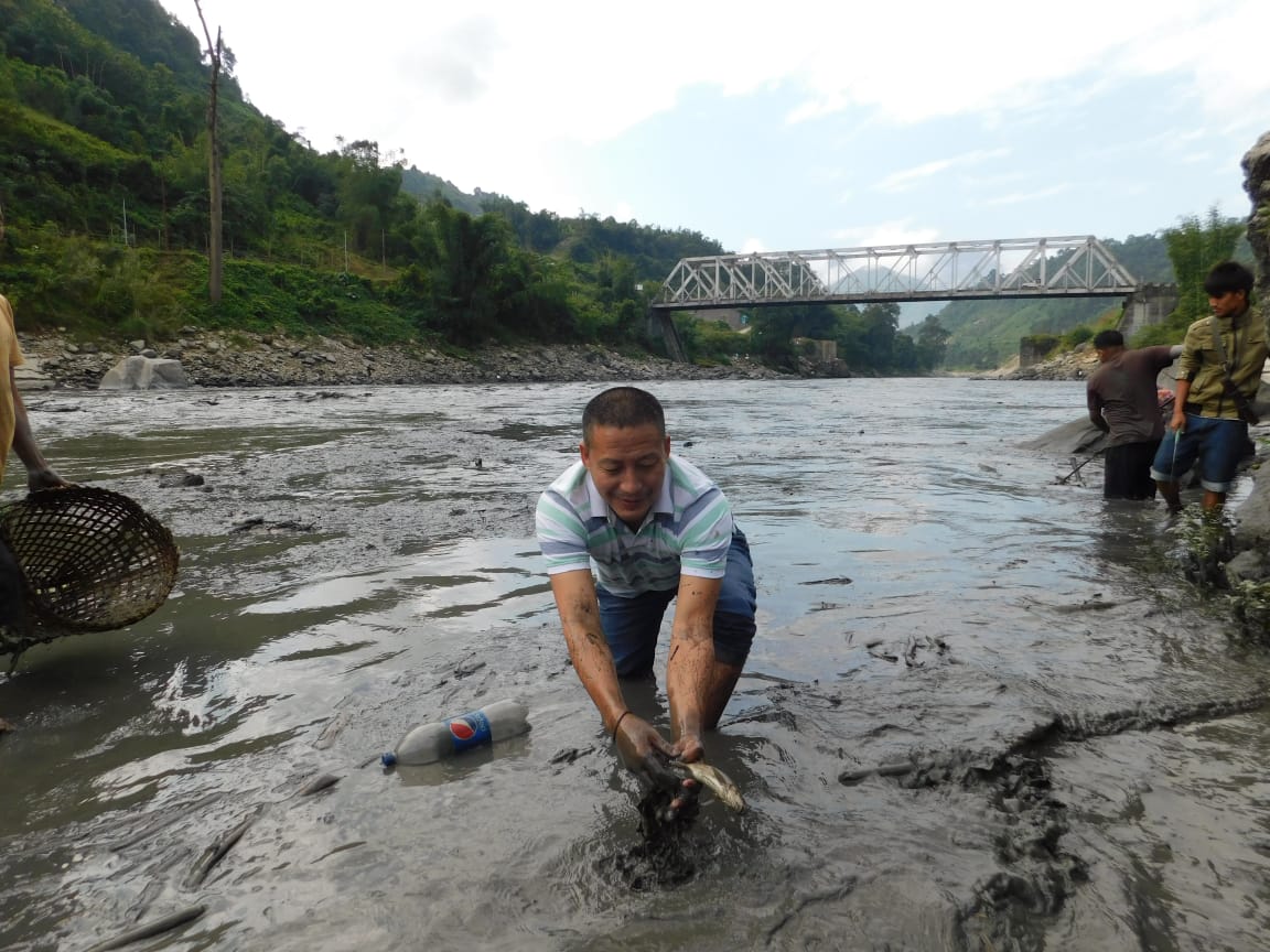 A man pulls a dead fish from the Kameng river in Arunachal Pradesh, India