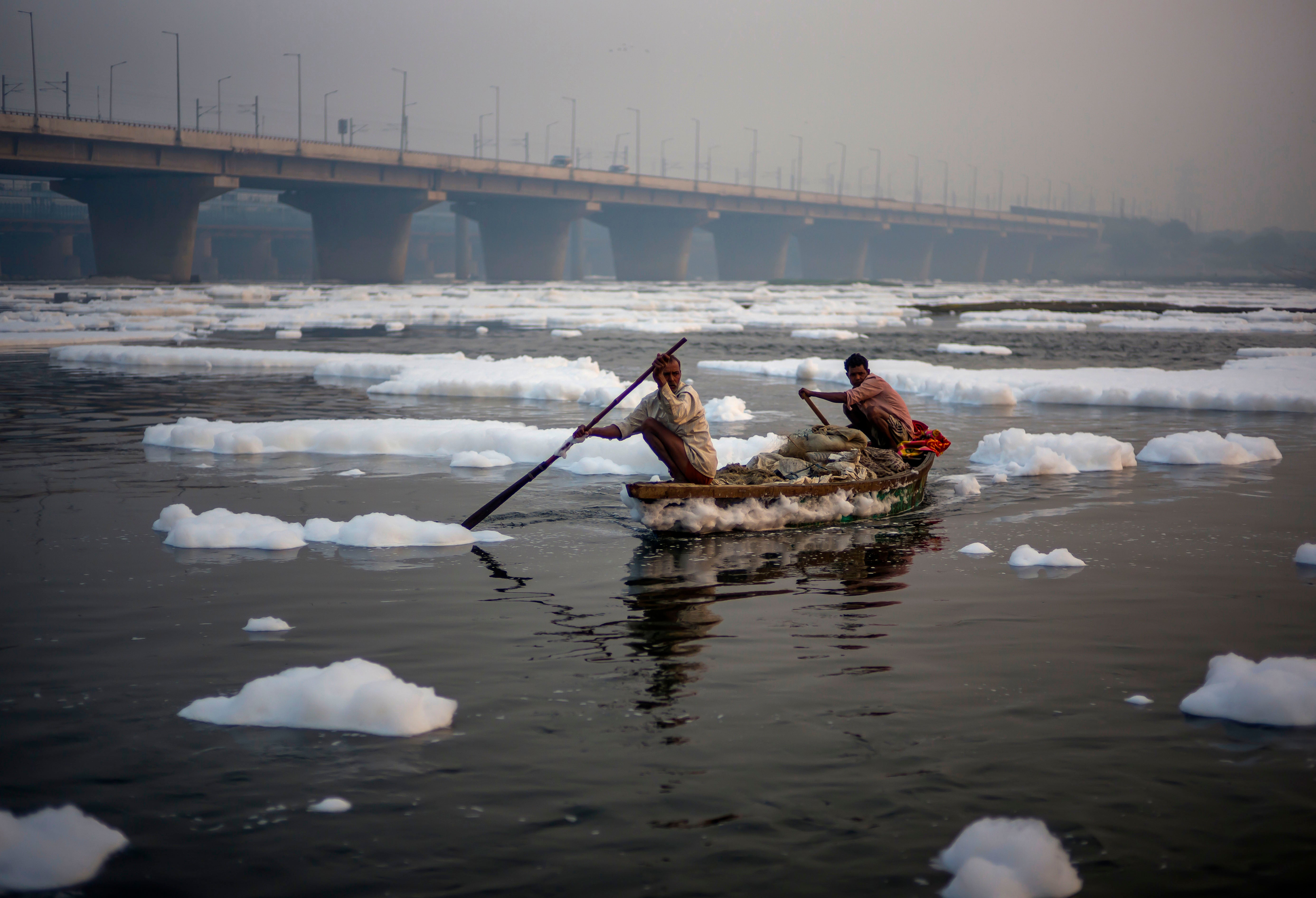 Fishermen row their boat on the waters of the Yamuna river amid the toxic foam caused by the pollution in the water as they return from a fishing trip on 9 November 2021