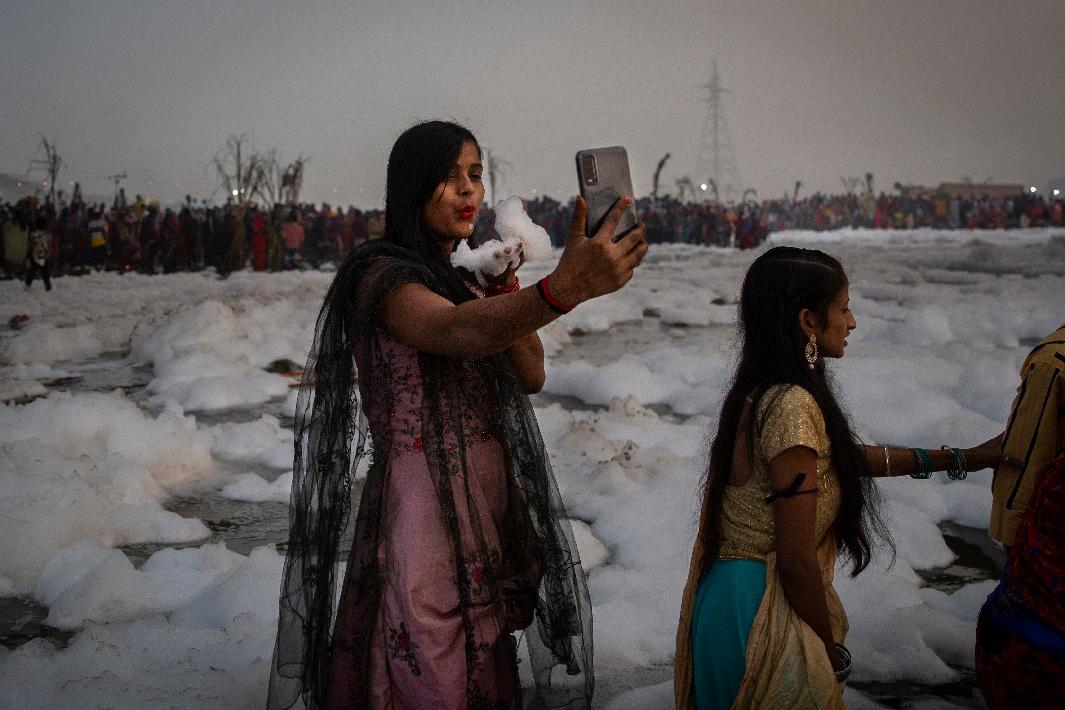 A Hindu devotee takes a selfie while holding handful of chemical foam she picked from Yamuna river during Chhath Puja festival in Delhi