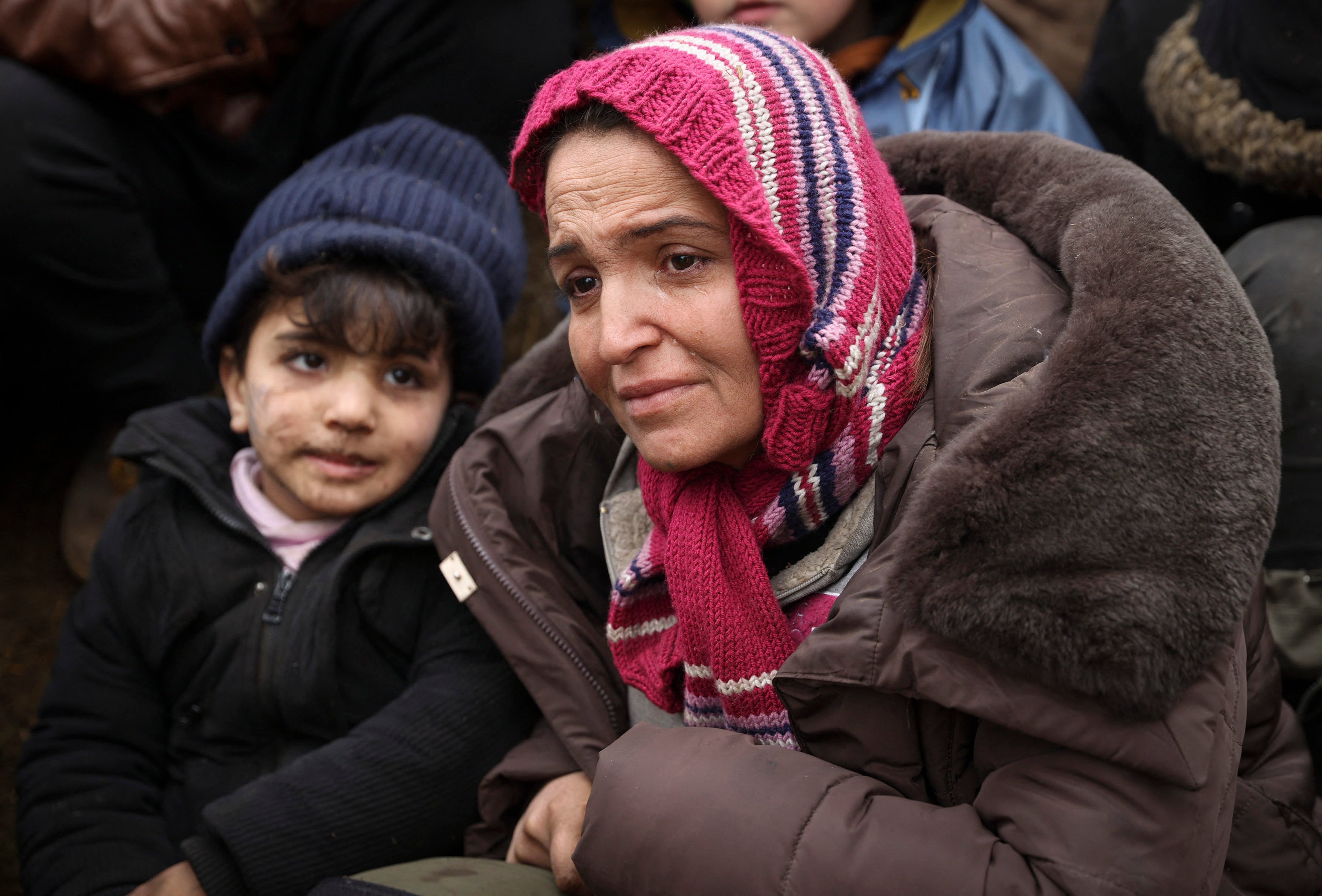 A woman and a child sit among a group of migrants in a camp near the Belarusian-Polish border