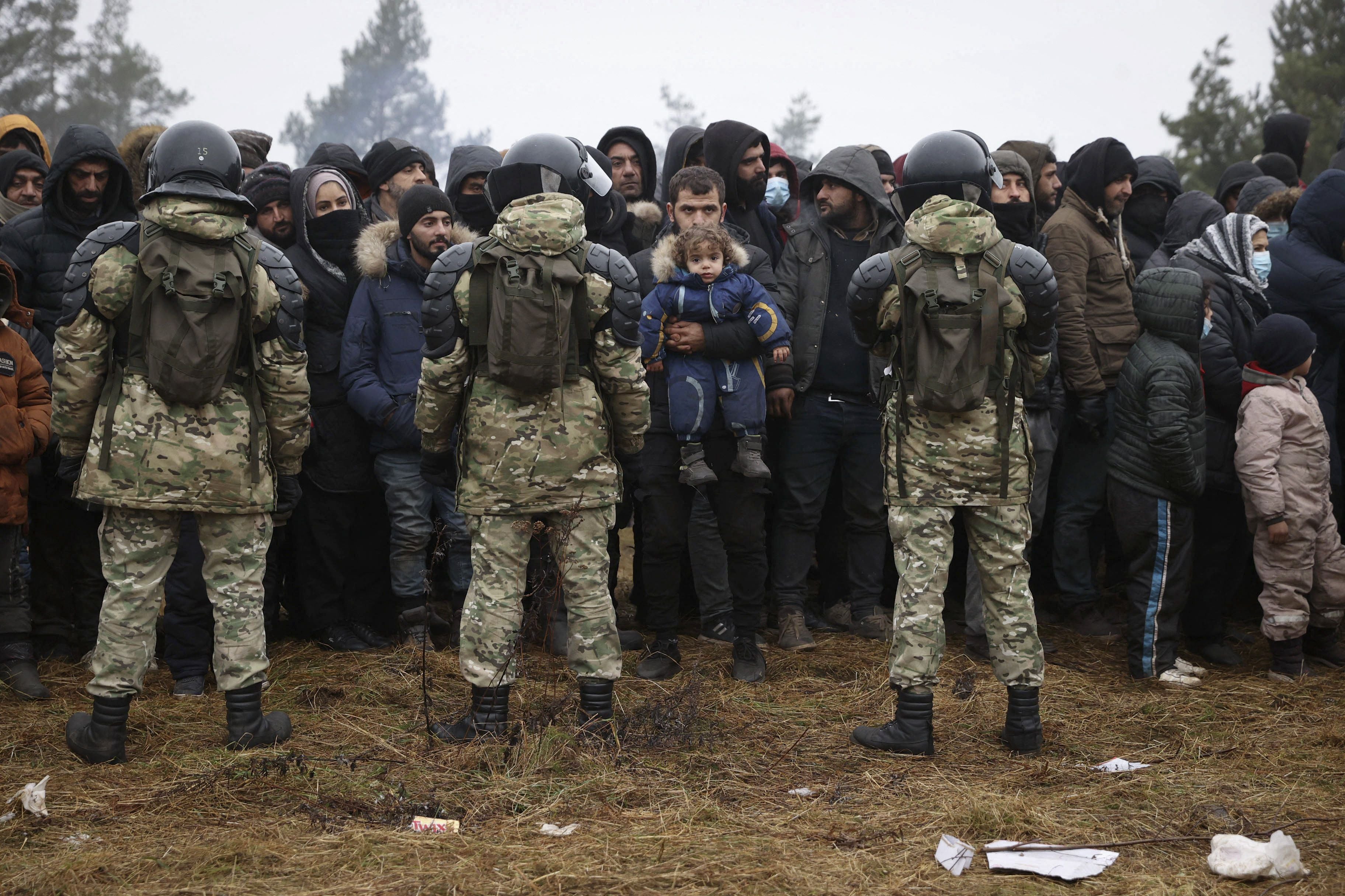 Belarusian service personnel stand in front of migrants at the border