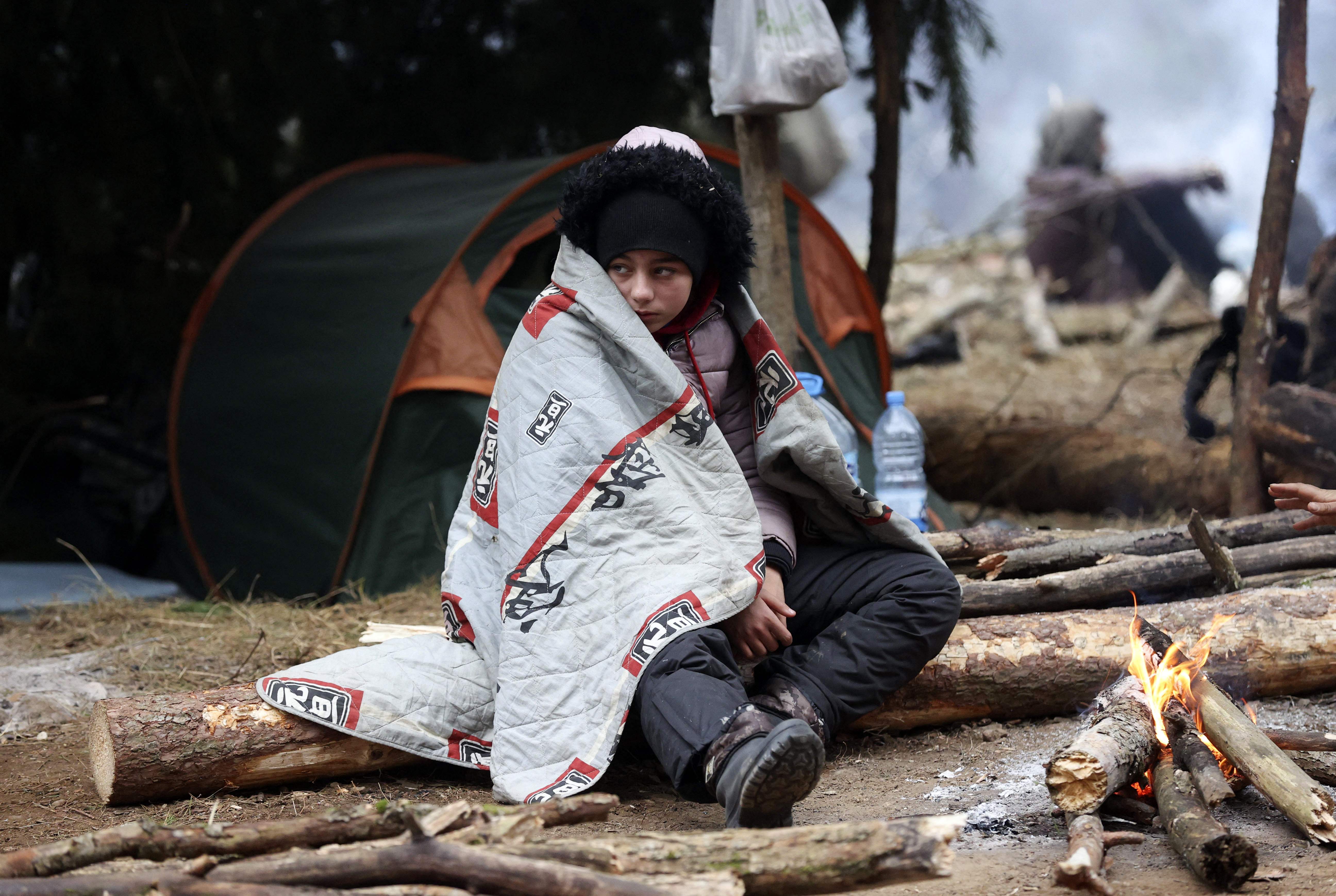 File: A migrant sits in front of a fire in a camp near the Belarusian-Polish border