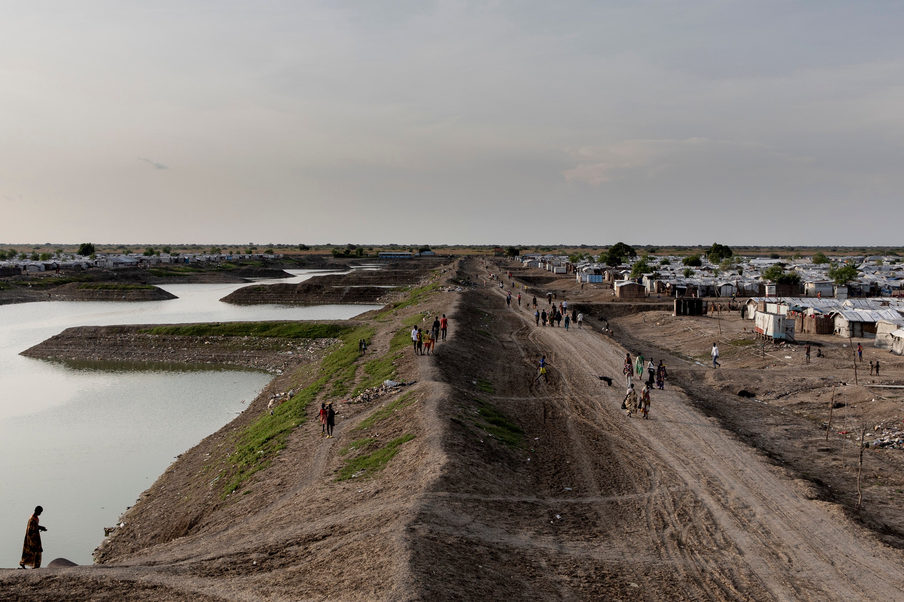 People walk past the basin where all excess water from the Bentiu displacement camp in South Sudan is collected