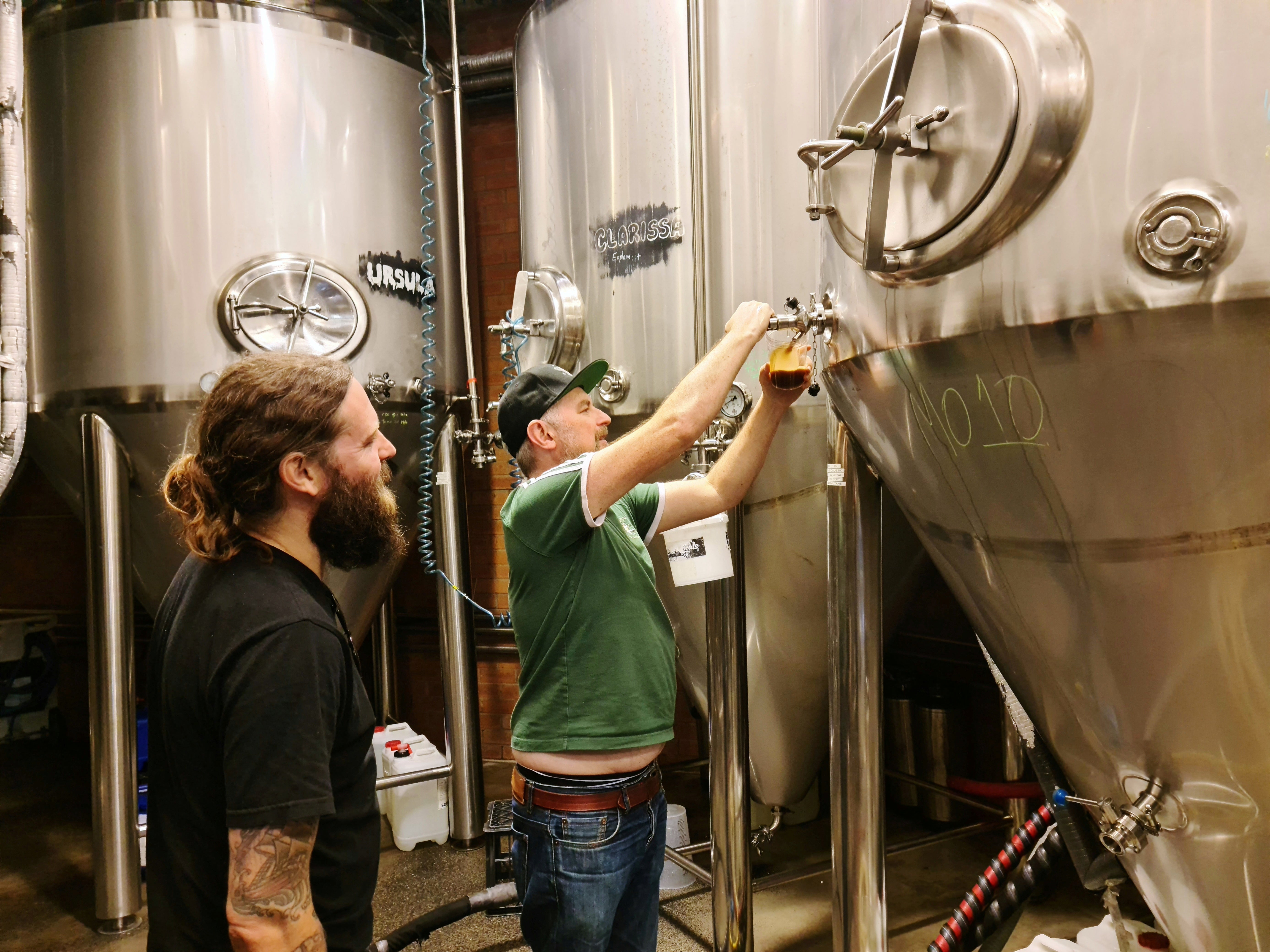 Young Henrys brewery co-founders Oscar McMahon (L) and Richard Adamson pour beer from their fermentation tanks at the brewery in Sydney, Australia