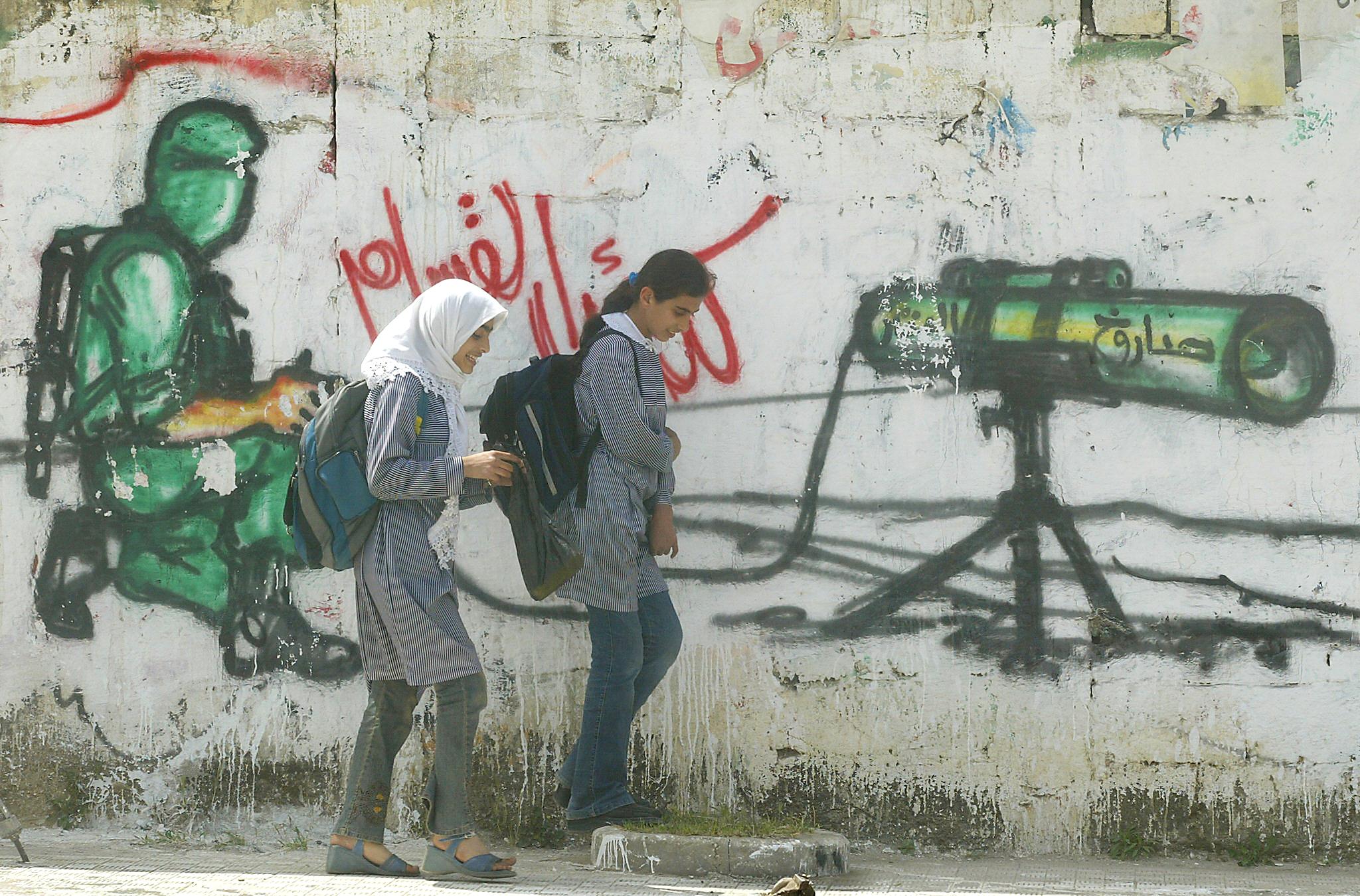 Two Palestinian school girls walk past graffiti supporting Hamas. The military wing of the group has been proscribed in the UK since 2001