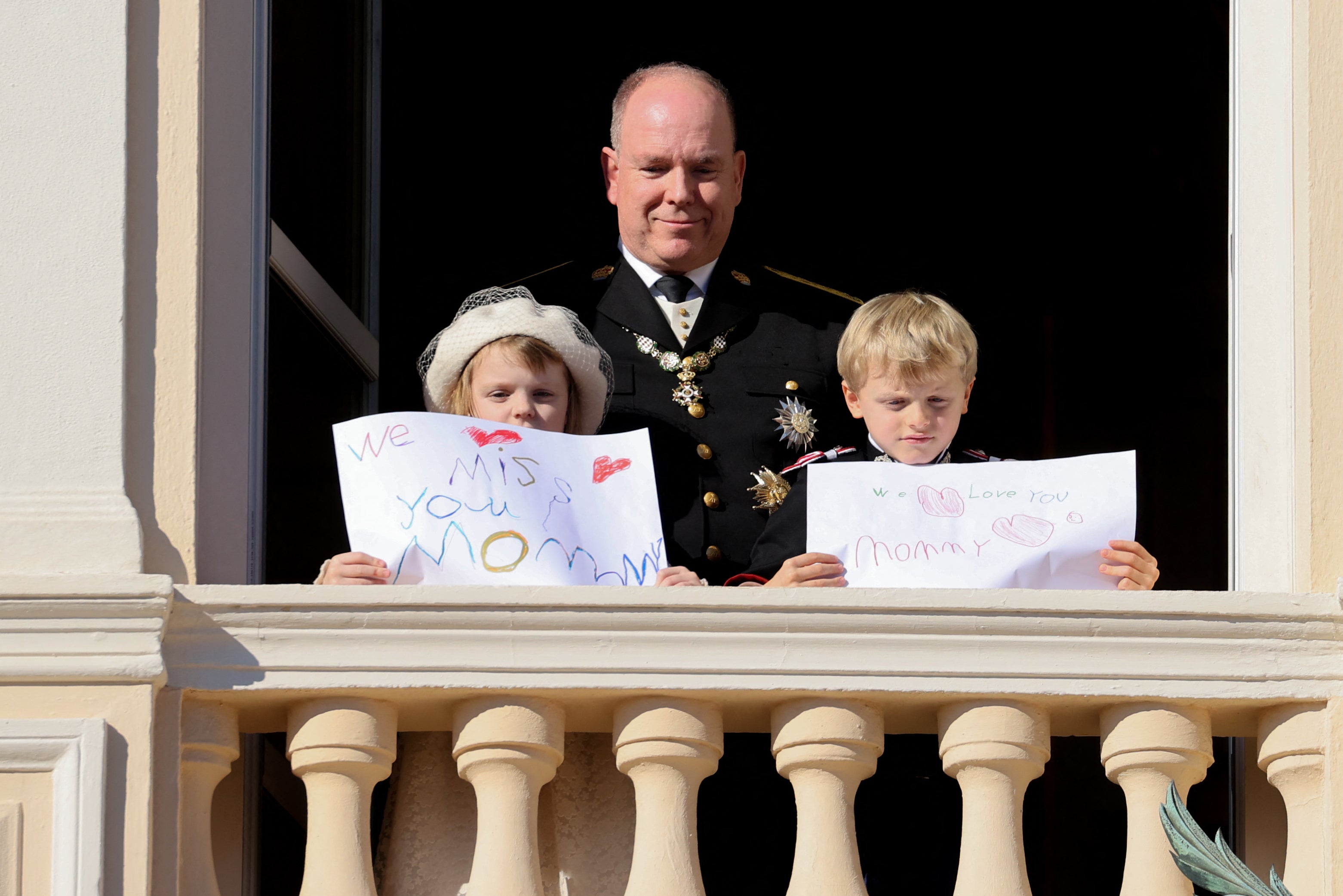 Prince Albert, Princess Gabriella (L) and Prince Jacques (R) stand with a message for Princess Charlene at the balcony of Monaco Palace