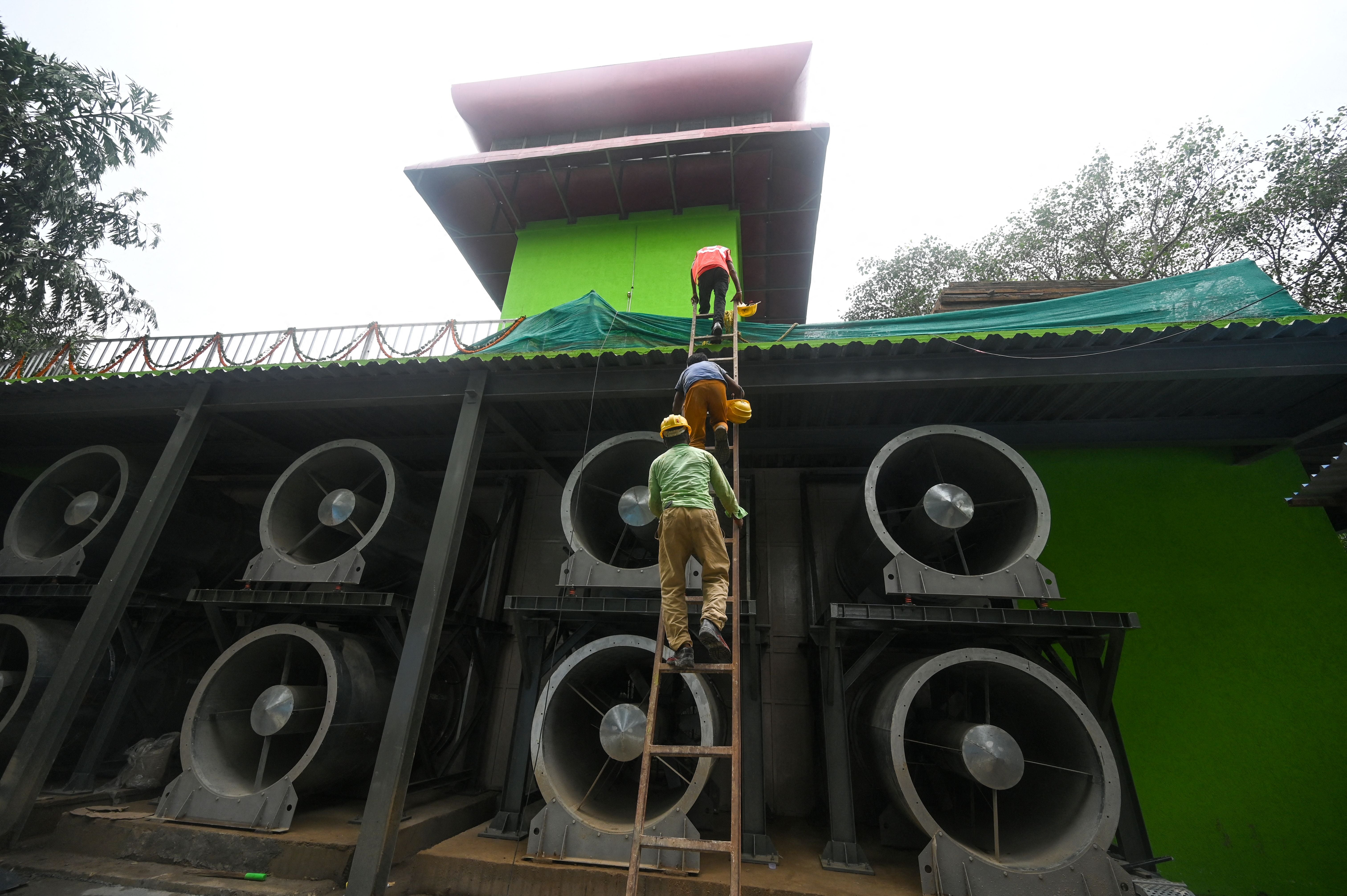 Workers climb a ladder at the 25-metre-high smog tower, built to purify the air during peak pollution season, in New Delhi