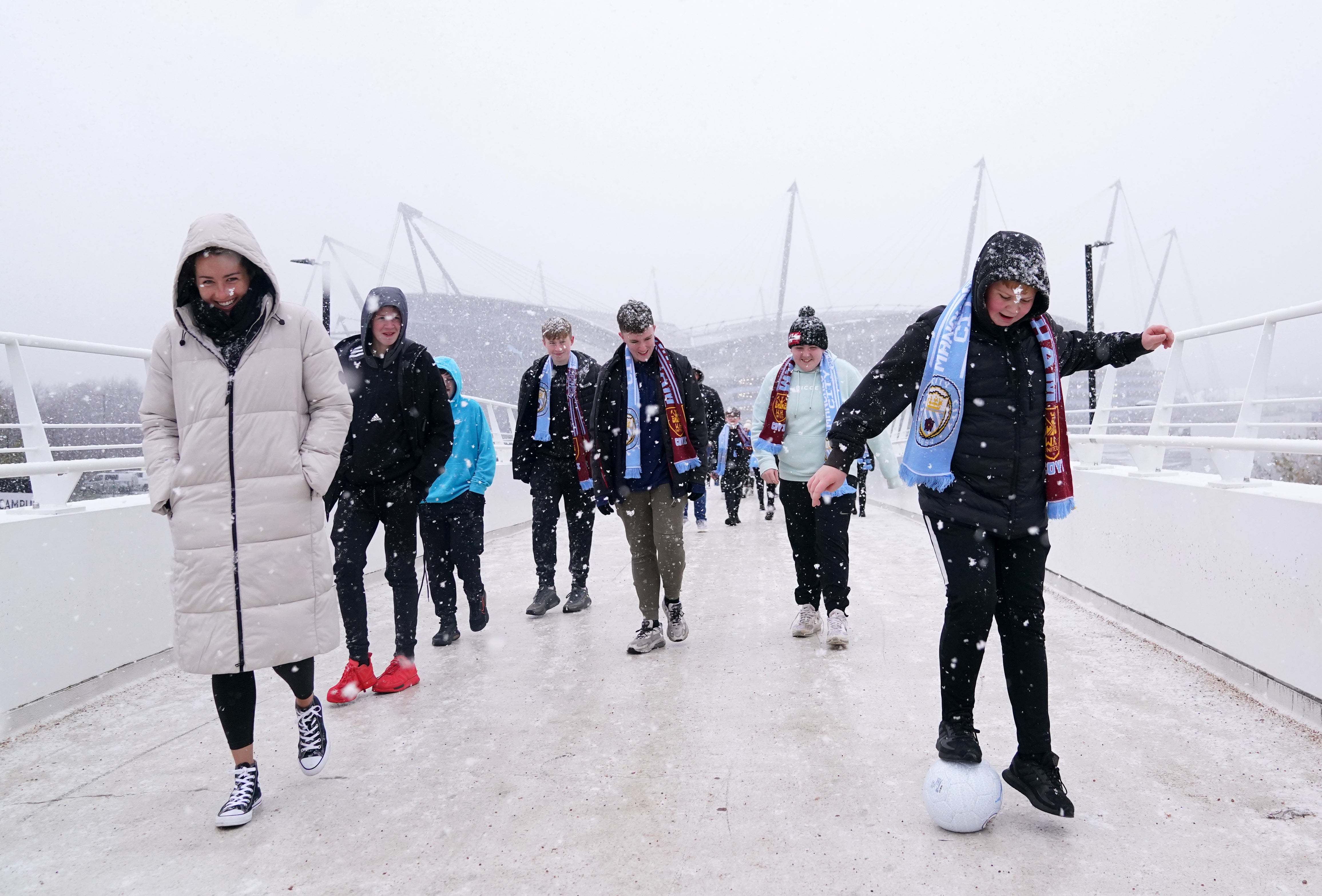 Fans cross the bridge to the Etihad Stadium in the snow before Manchester City’s game with West Ham (Martin Rickett/PA)