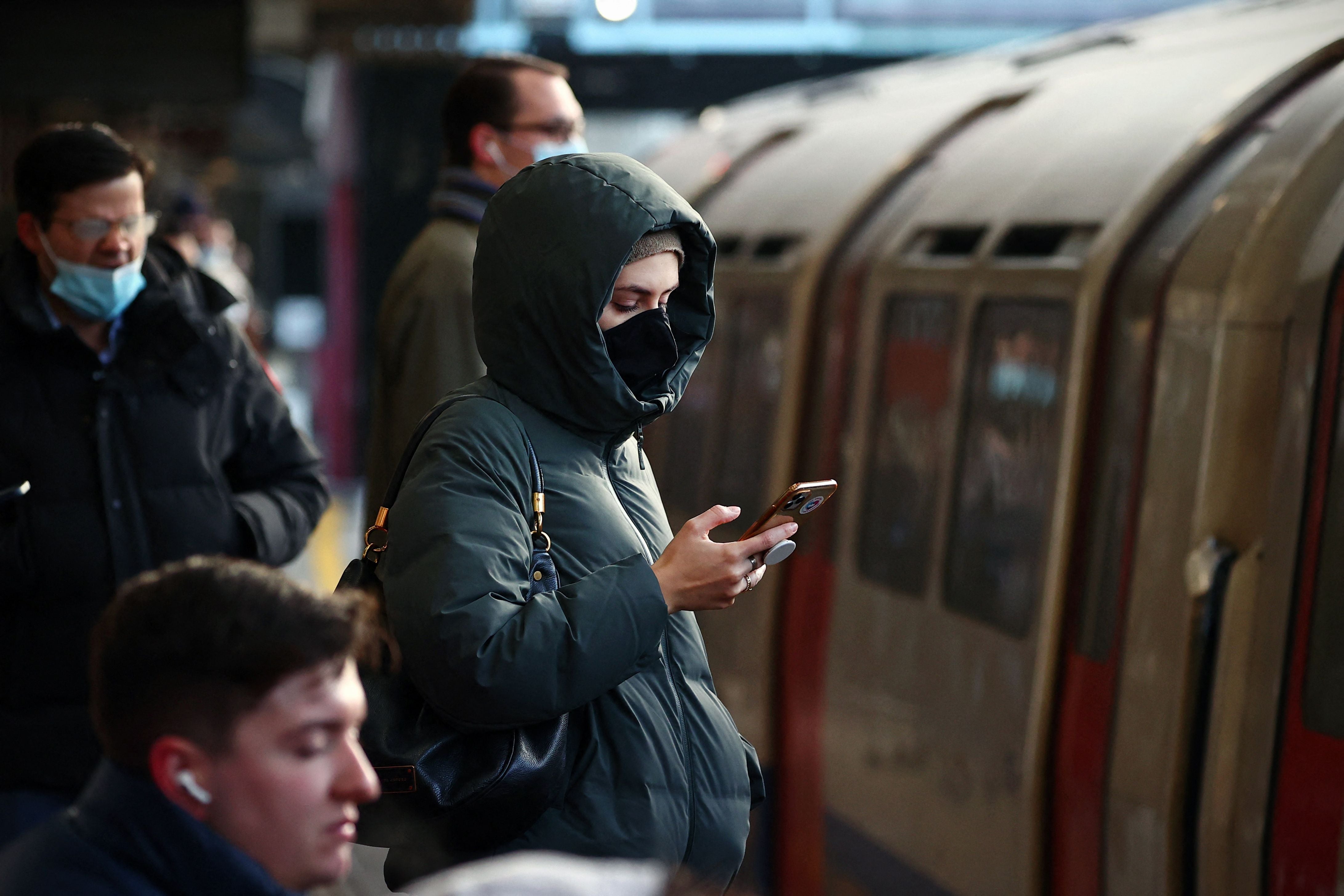 Commuters wait on a platform at Barons Court Underground station a day before masks will be made compulsory again