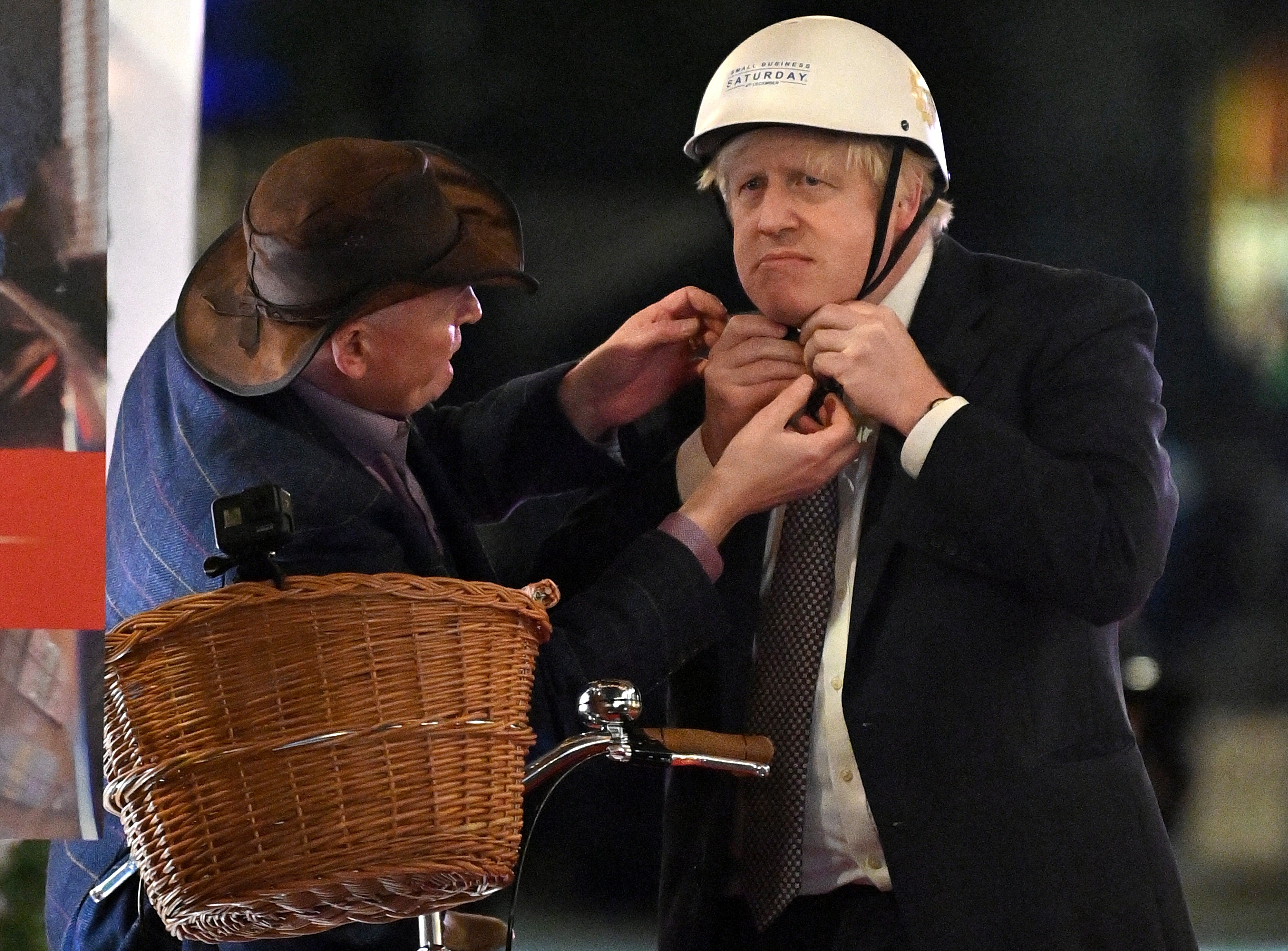 Prime Minister Boris Johnson receives help as he puts on a bicycle helmet before riding a bike as he visits a UK Food and Drinks market which has been set up in Downing Street, London. Picture date: Tuesday November 30, 2021.