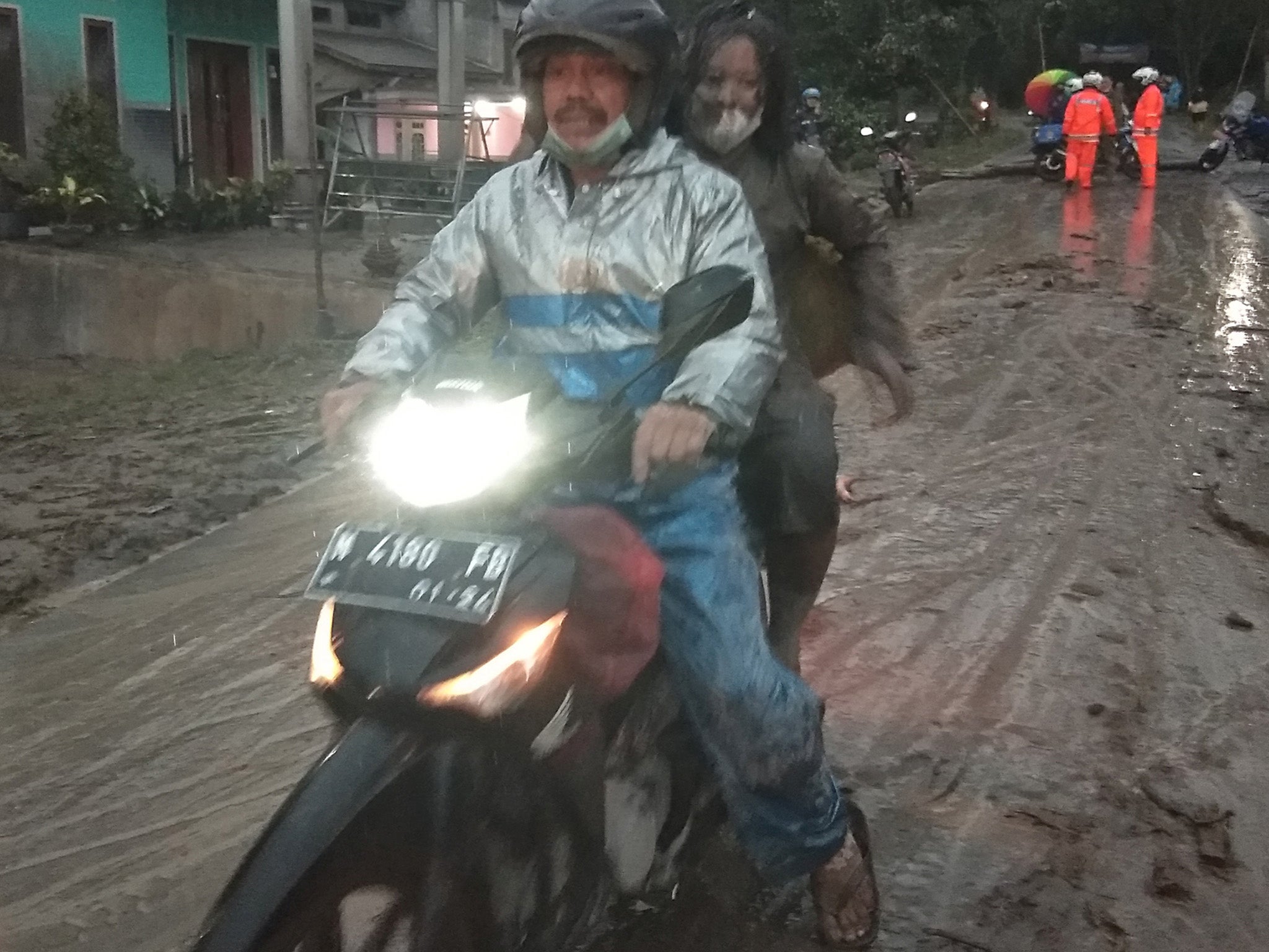 A pair ride a motorbike on a road covered with volcanic ash