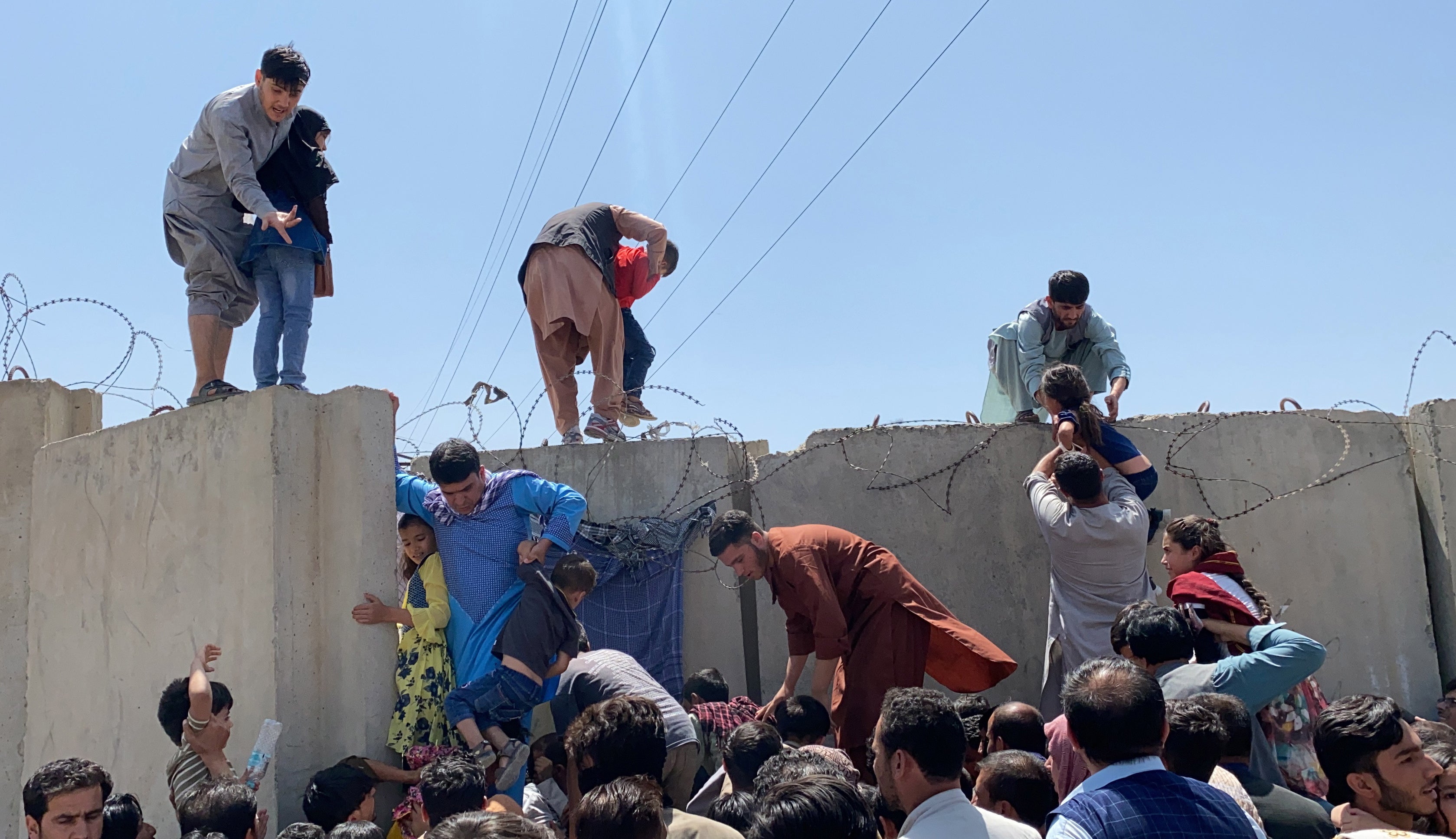 People struggle to cross the boundary wall of Hamid Karzai International Airport to flee the country